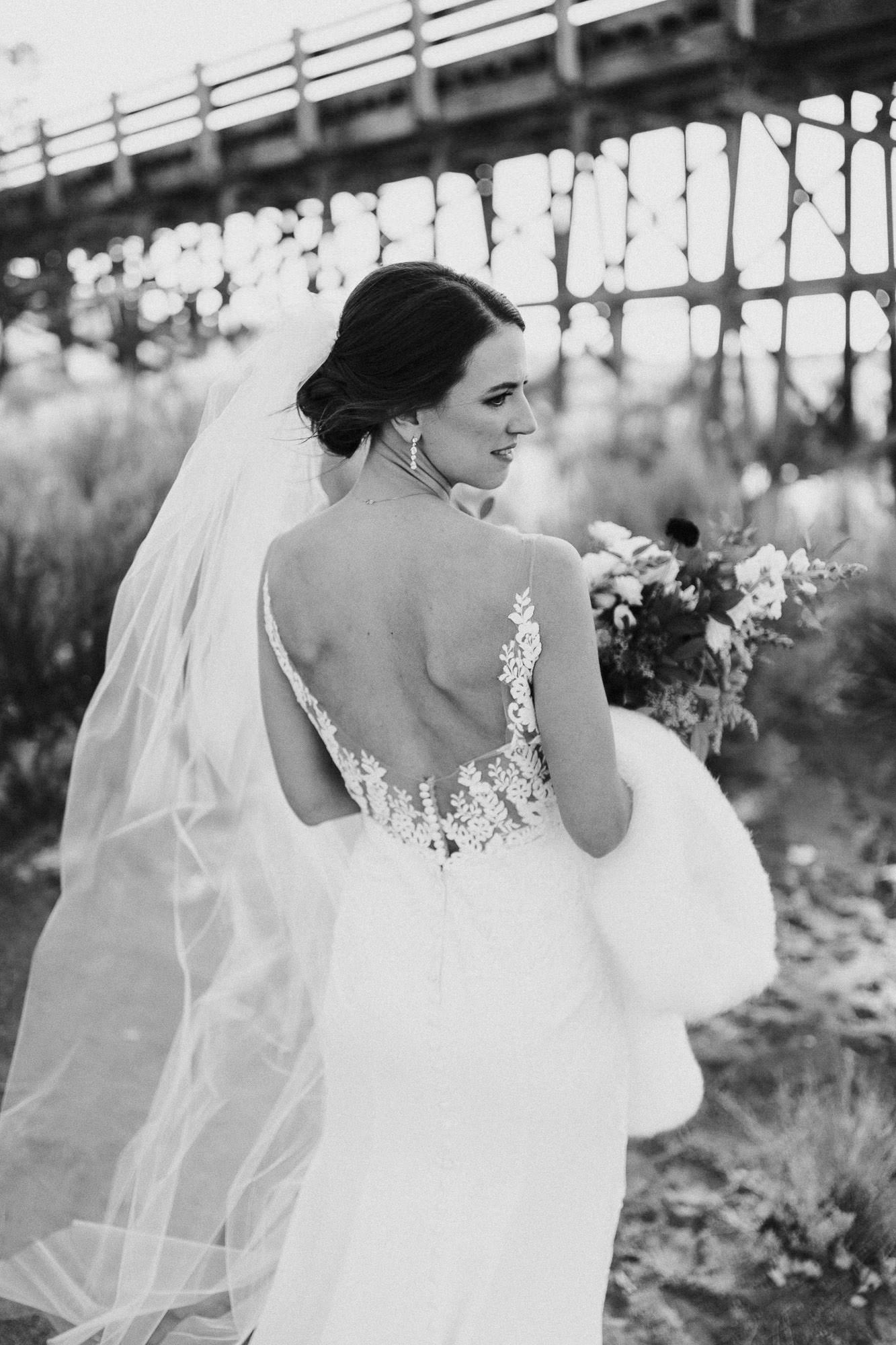 Bride shows back of dress for portrait in front of trellis bridge at Brasada Ranch in Oregon