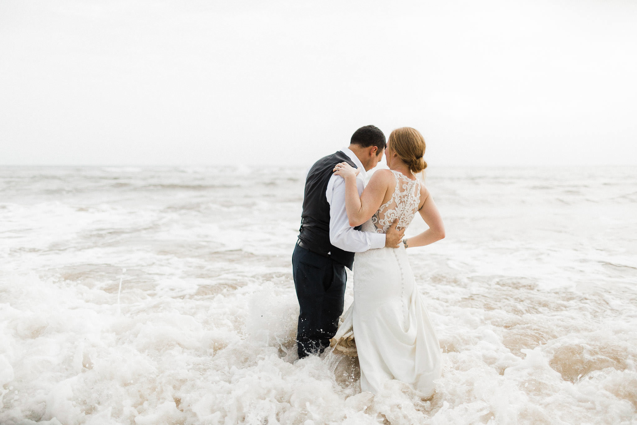 Bride and groom wade into the surf on a beach on Kauai, Hawaii