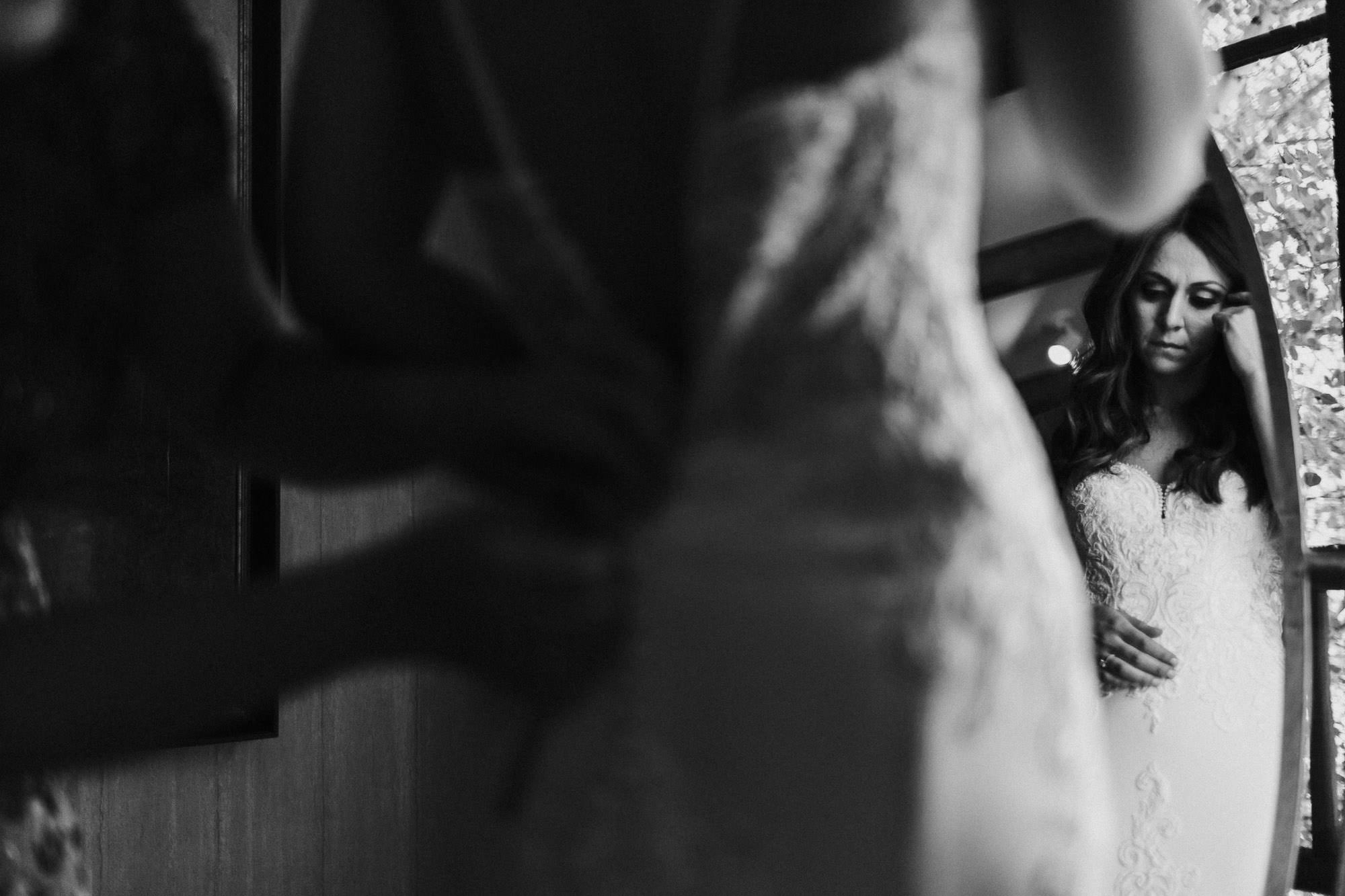 Bride looks in mirror as her mom buttons her dress at Sunriver Resort in Oregon