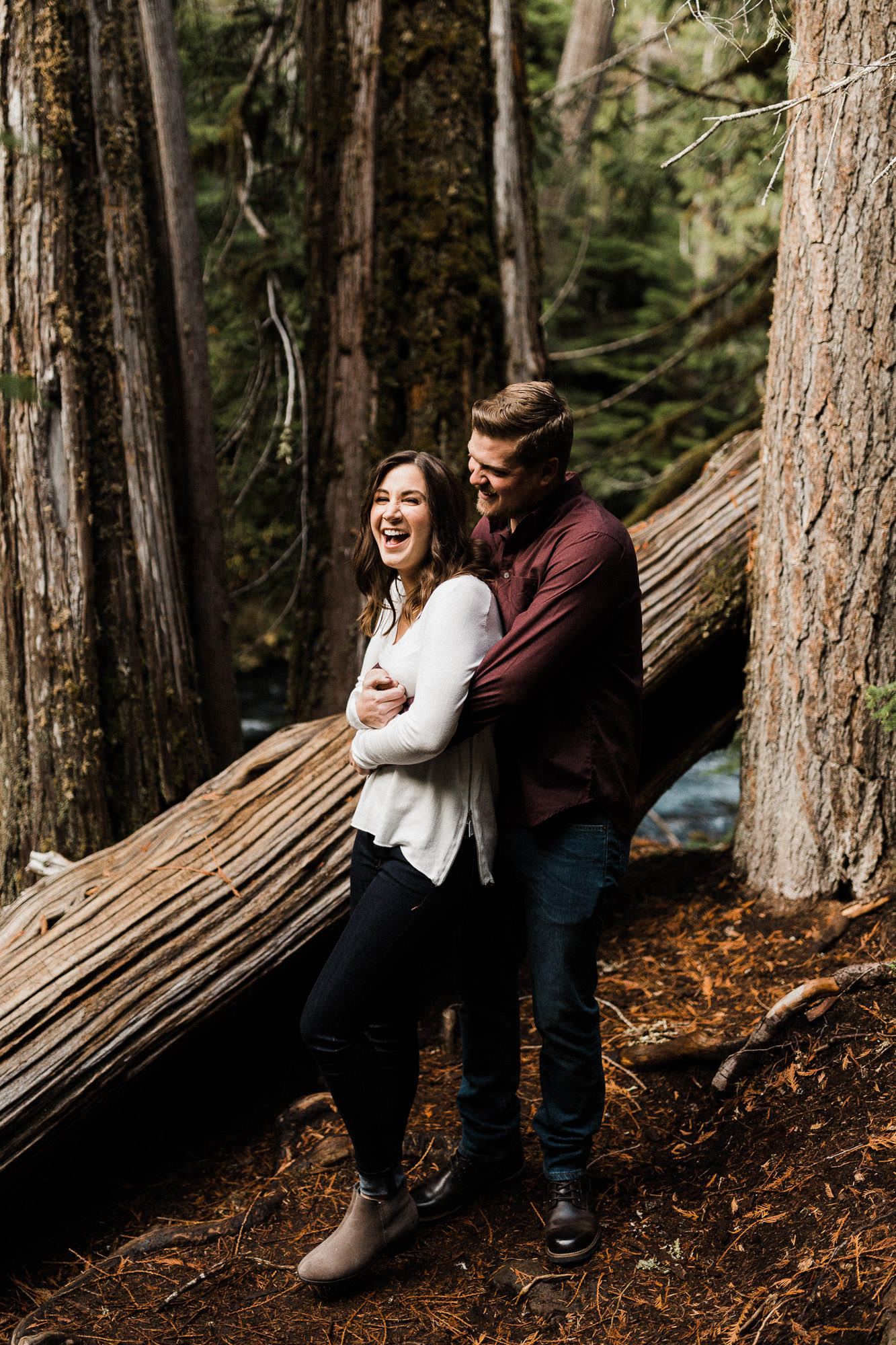 Man embraces laughing fiancee in a forest on the McKenzie River in Oregon