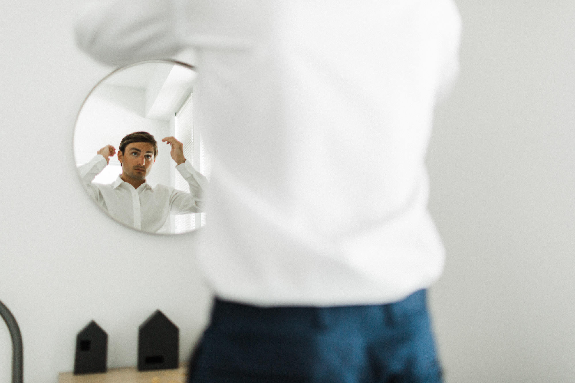 Groom's face reflected in circular mirror as he adjusts his hair