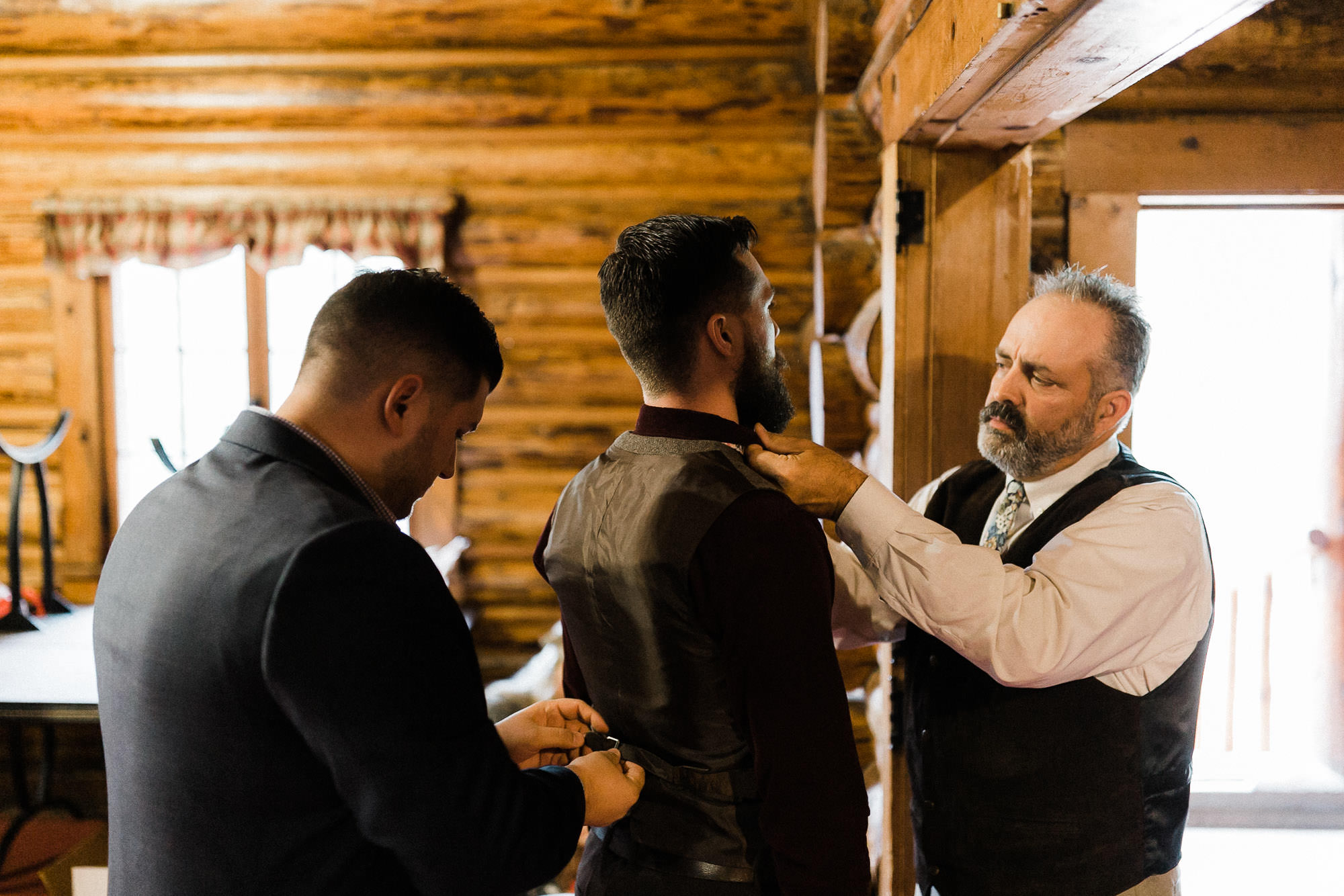 Dad and guest help groom with is tie and vest at Skyliner Lodge