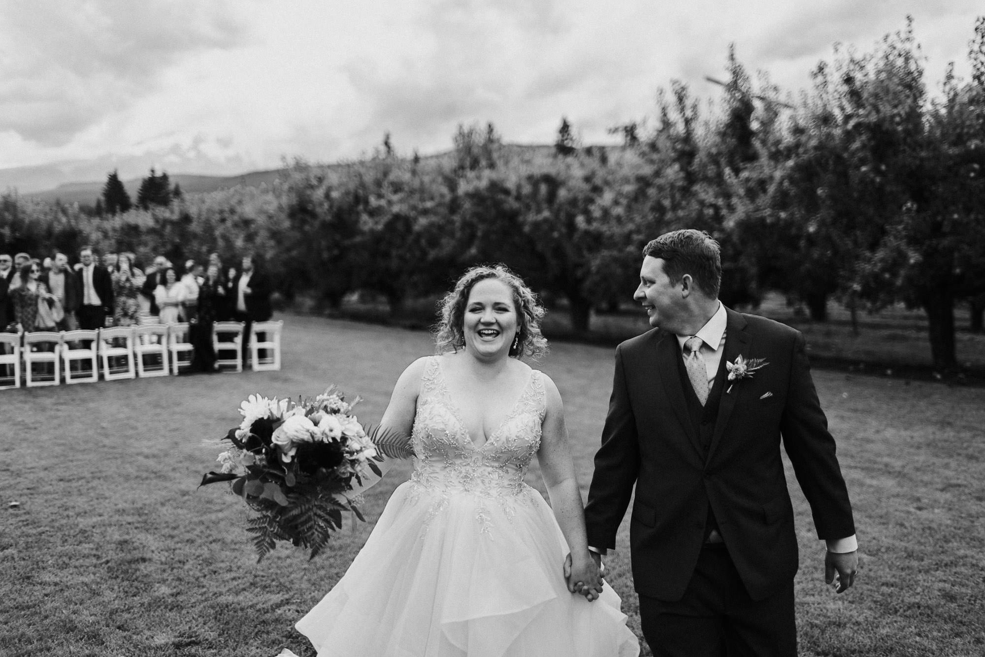 The bride beams while the groom looks back at the guests as they leave the ceremony.