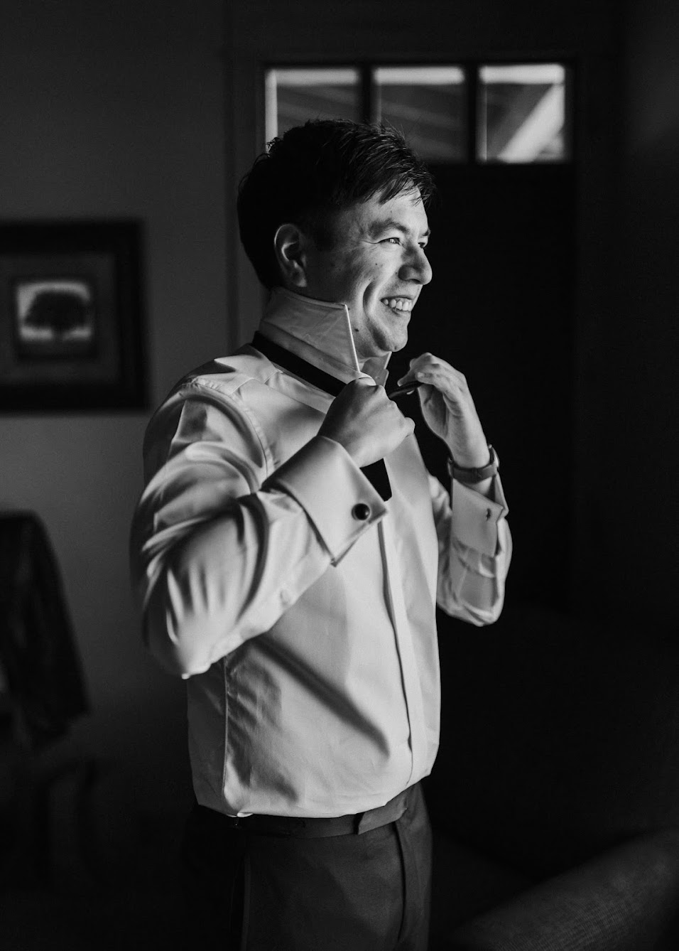 Grooming getting ready for his wedding day. He has a big smile on while tying his bowtie. 