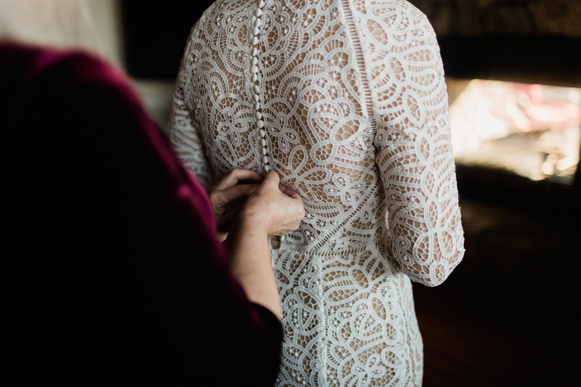 Mother of the bride buttoning the top of the bride's wedding dress. 