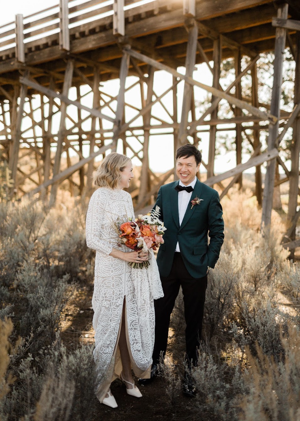 Bride and groom share a laugh while they walk through the bushes 