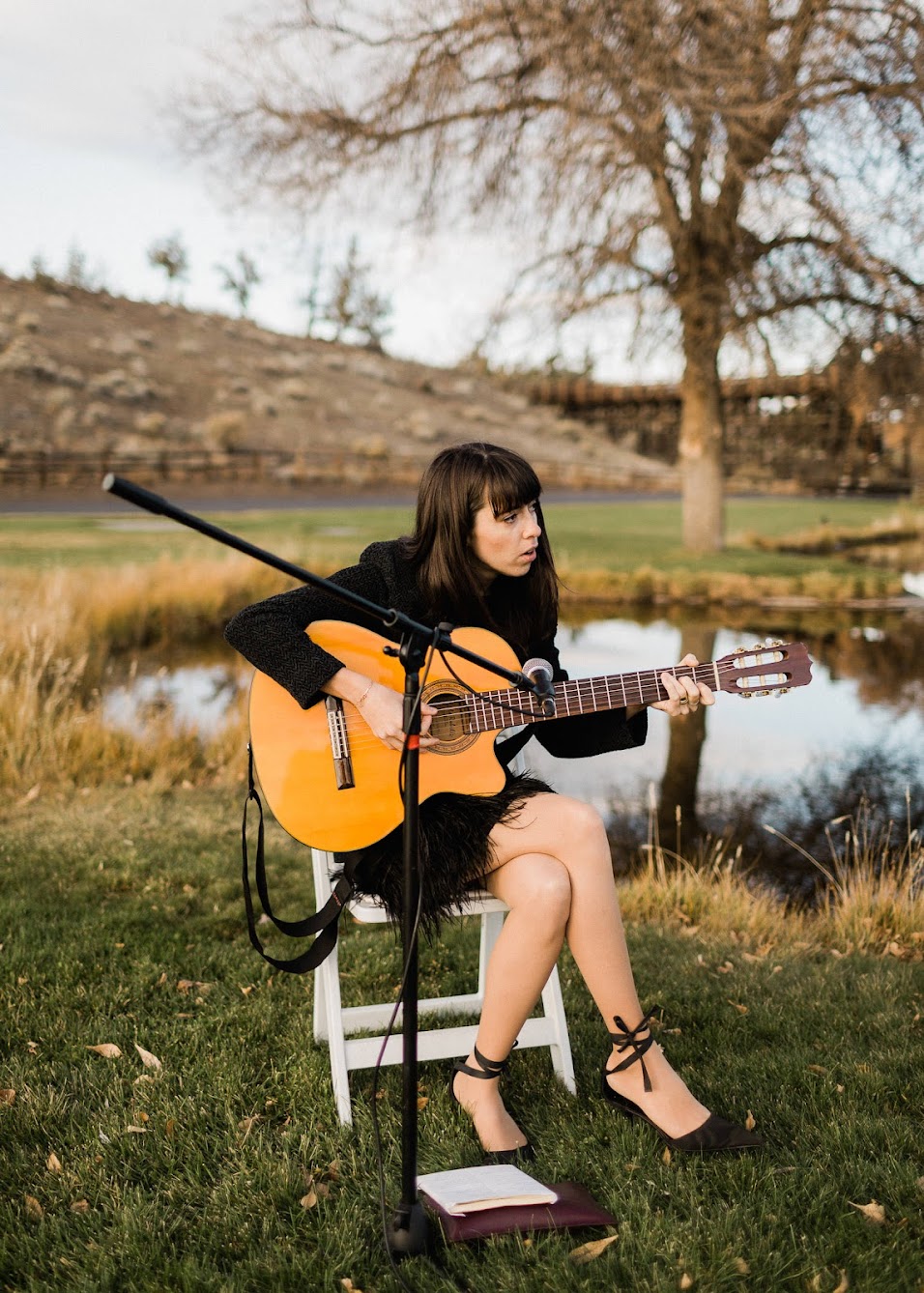 A women guitarist, sitting in a chair playing music while for the ceremony.