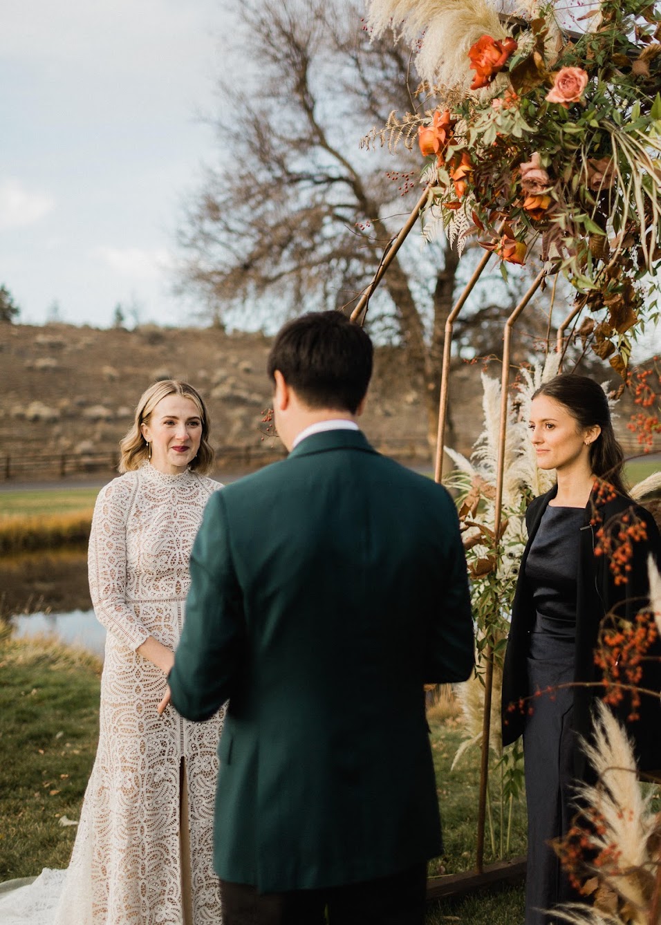 The bride and officiant both watching the groom while he reads his vows to the bride.