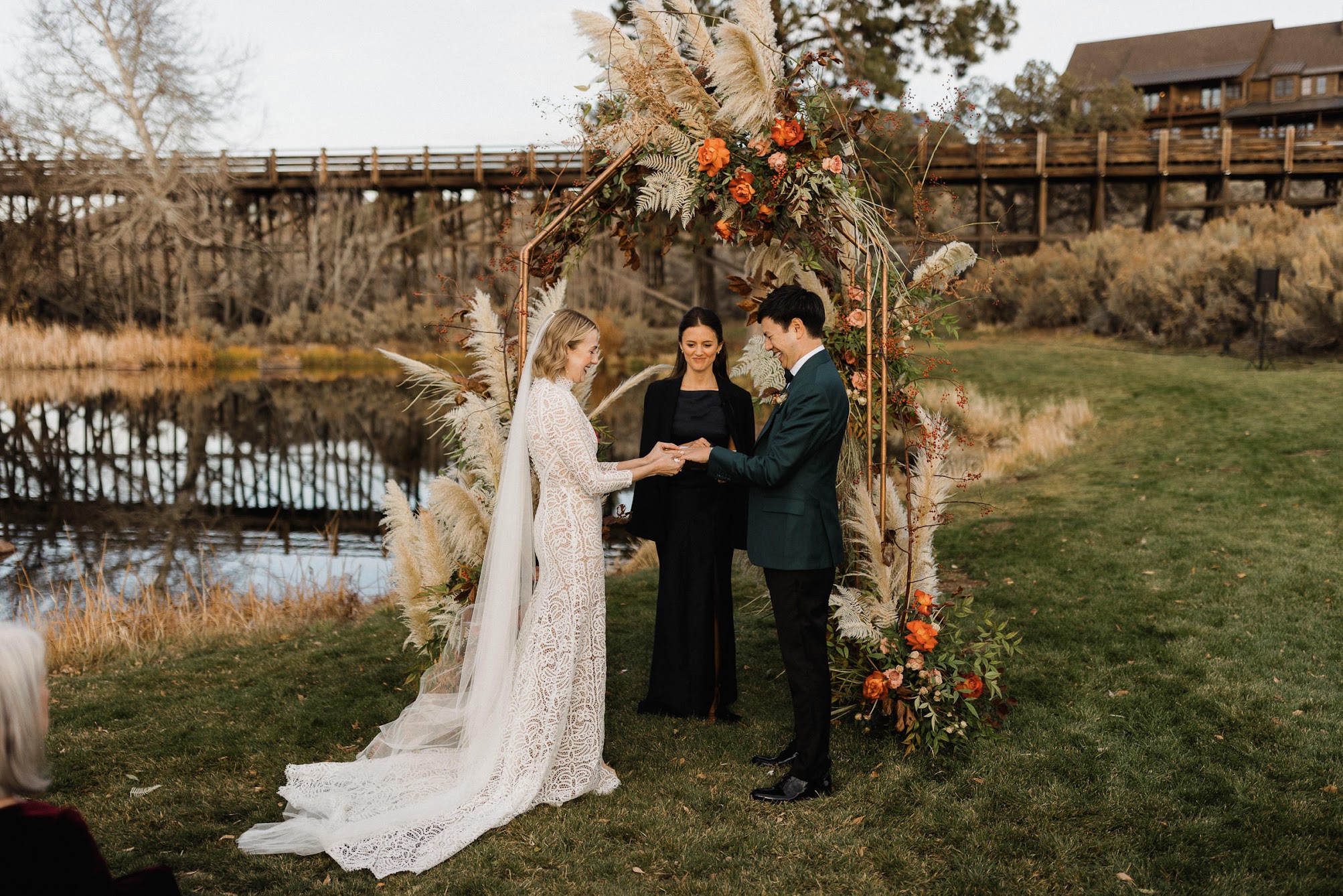 The bride is putting on the groom's wedding ring in front of the arbor.