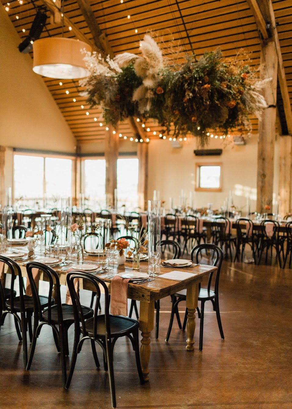 A large floral install hanging in the Brasasa wedding venue above farm tables with black bentwood chairs.