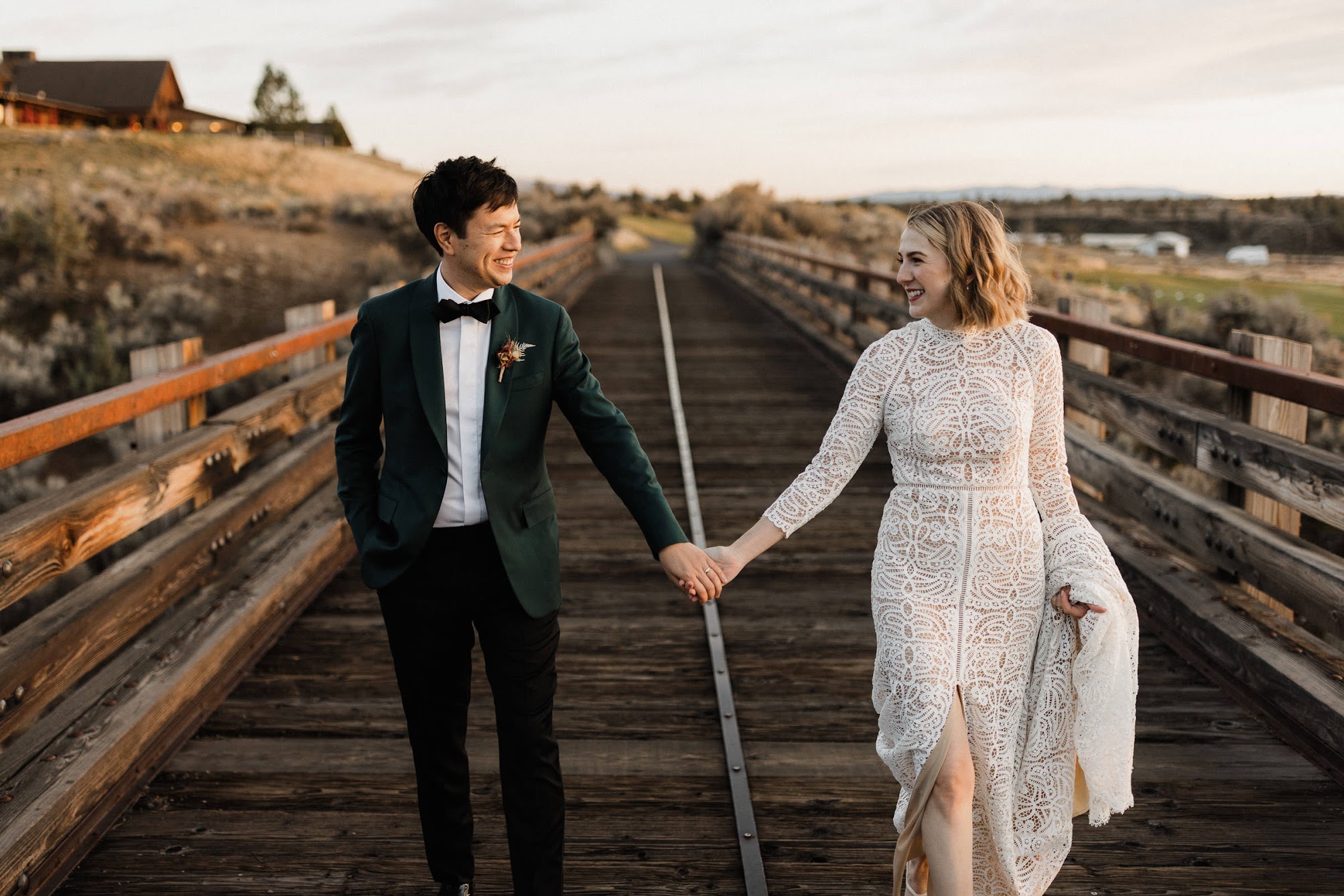 the bride and groom looking at each other while they hold hands on a wooden bridge.
