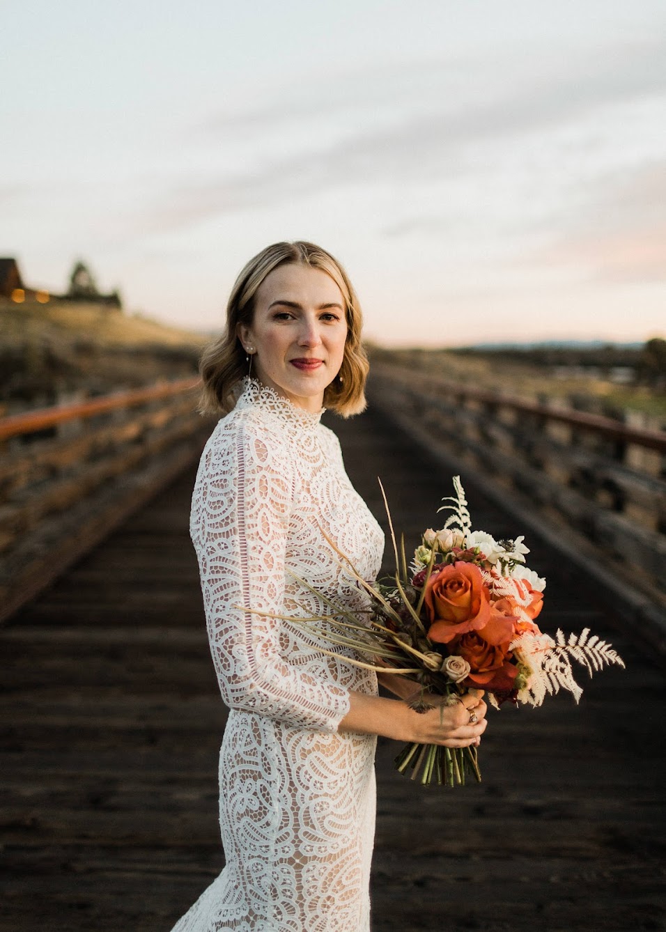 The bride looking into the camera, standing sideways hold her bouquet standing on a bridge.