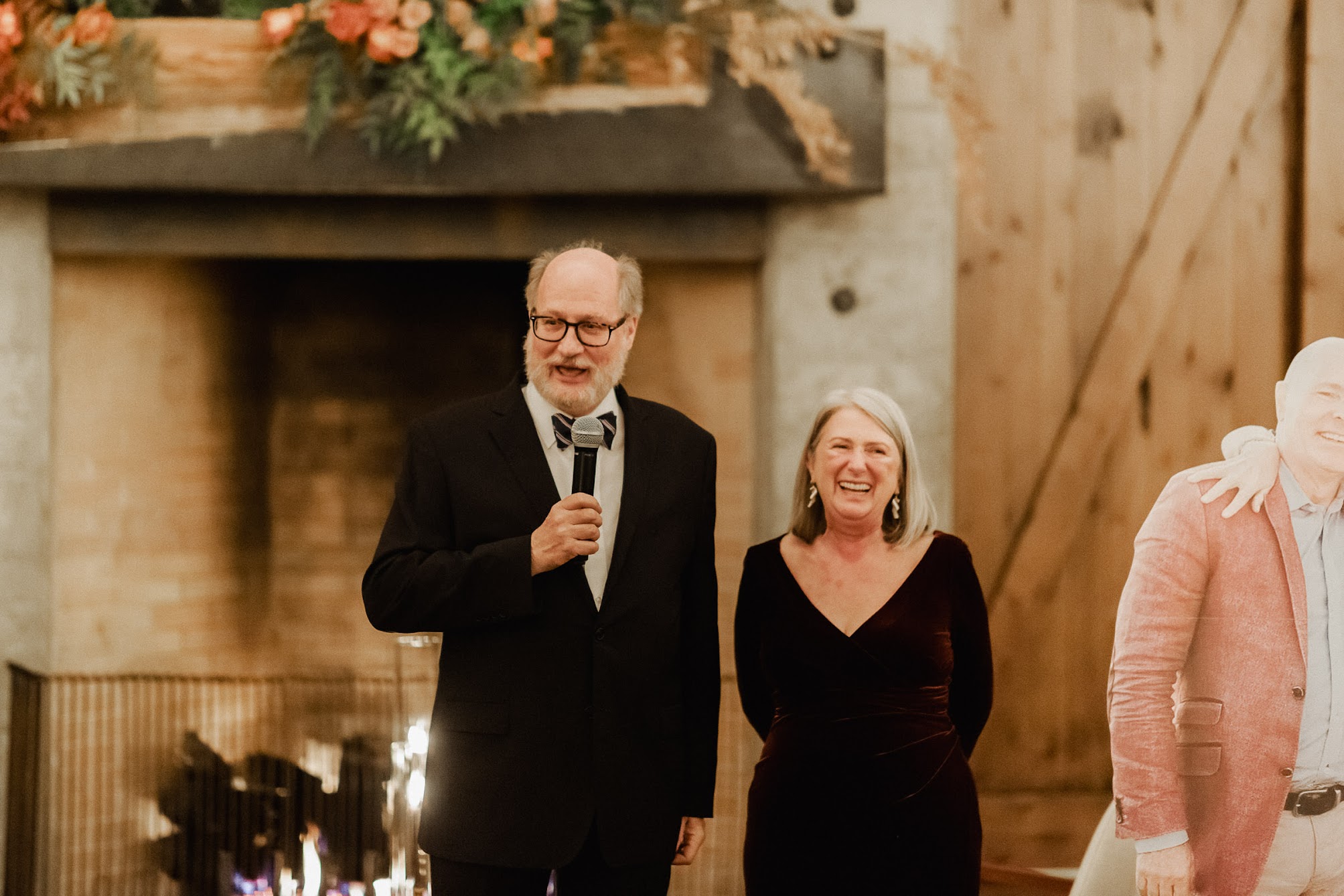 father and mother of the groom standing in front of the fireplace giving a speech. 