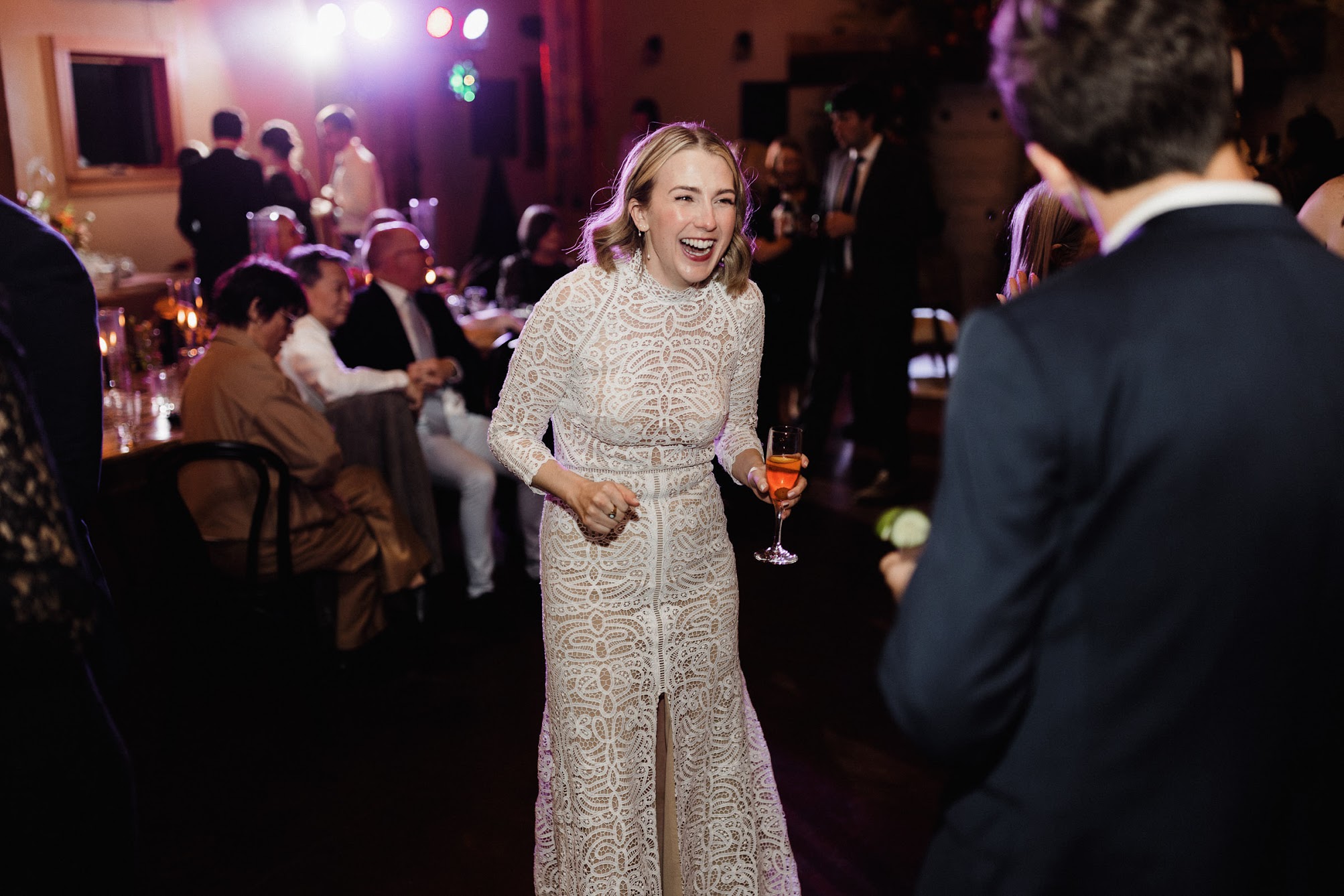 The bride holding a drink, laughing while on the dance floor