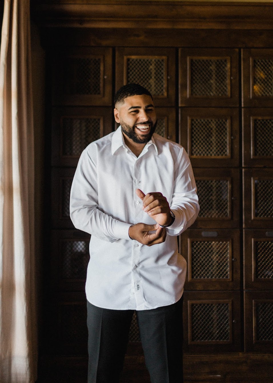 the groom getting ready for his day, as he smiles and buttons his shirt. 
