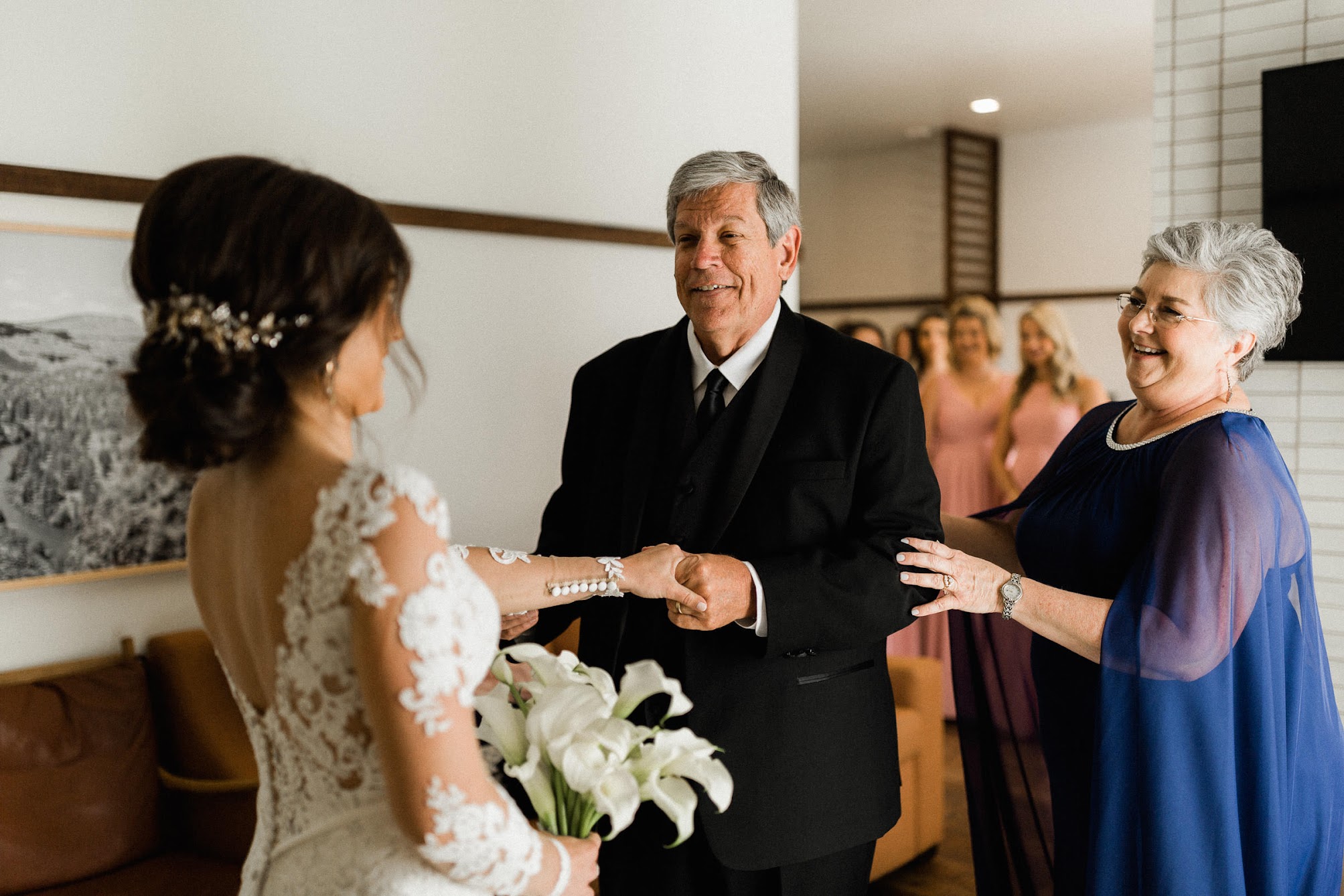 dad, mom, and daughter. Dad is holding his daughter's hand, as she stands in her wedding dress. 