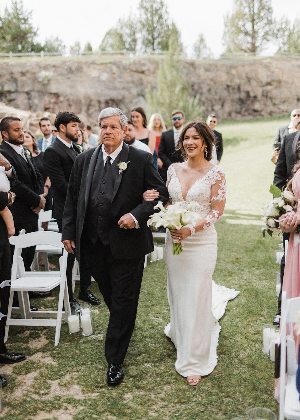 Bride walking down the aisle with her dad. The guests are standing watching. them walk down 