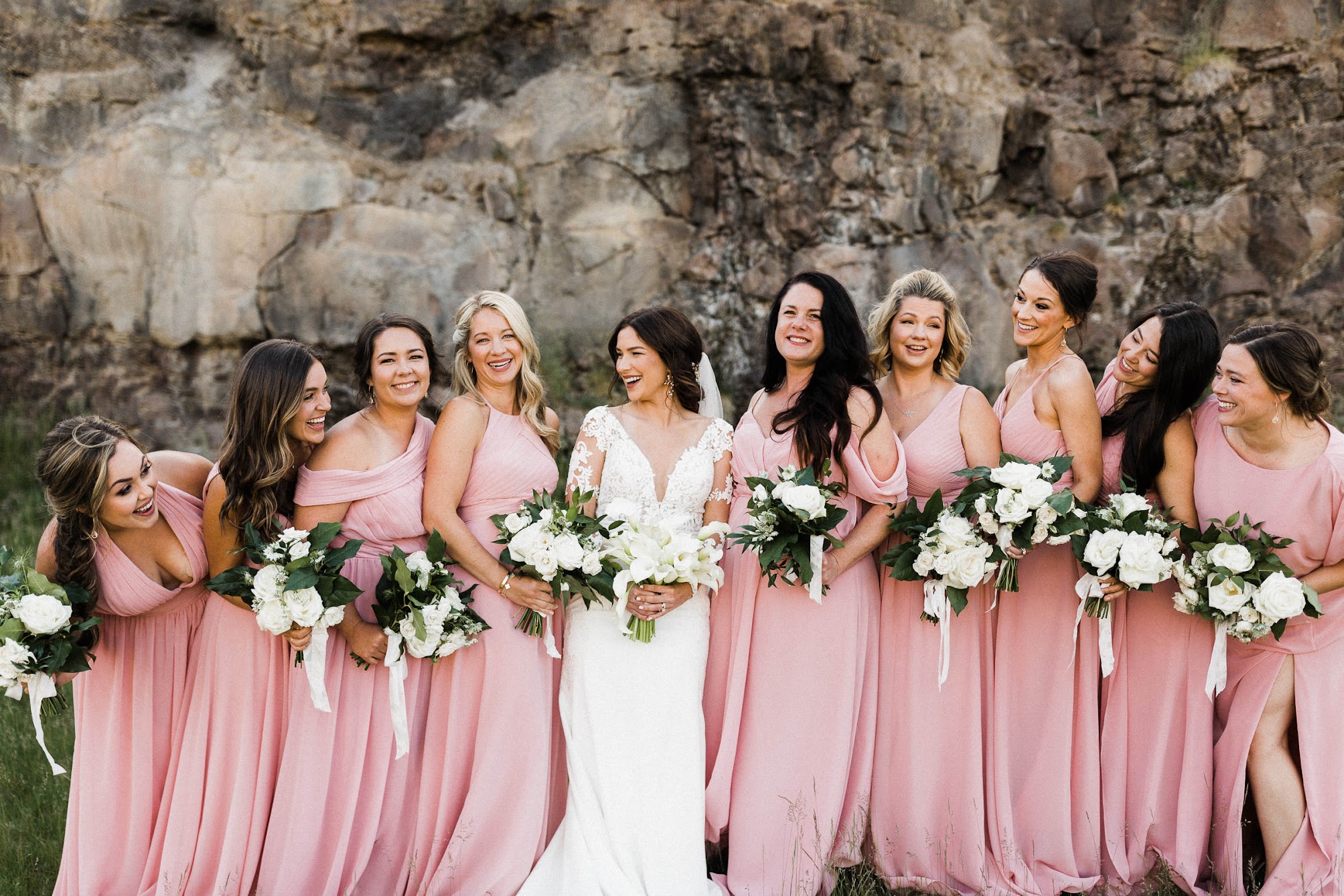 the bridesmaids in long flow-y dresses holding their bouquets and the bride is in the middle of them