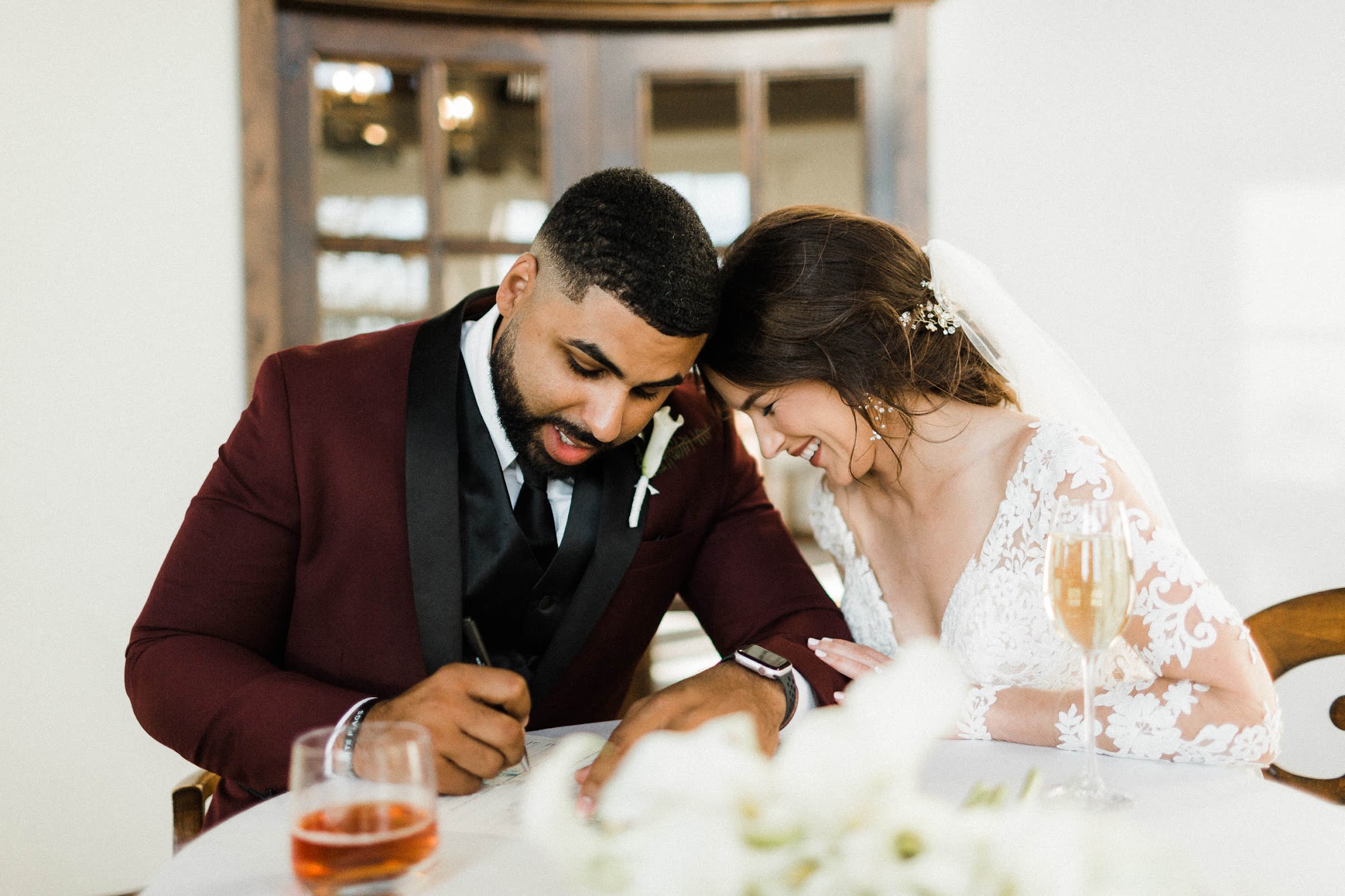 couple signing their marriage certificate, leaning in with their heads touching 