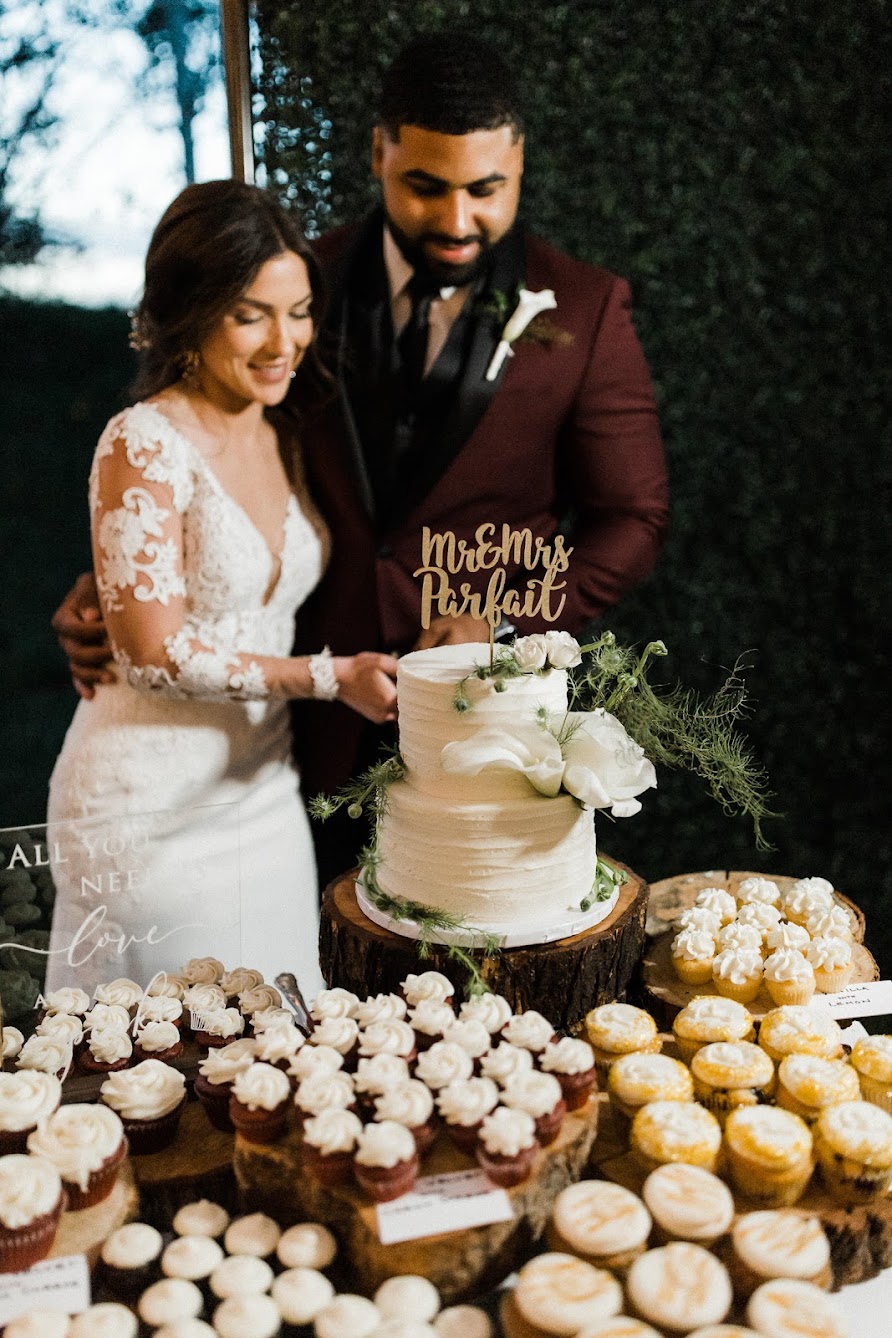 the bride and groom cutting into their two tired cake with a bunch of mini cupcakes around the wedding cake.