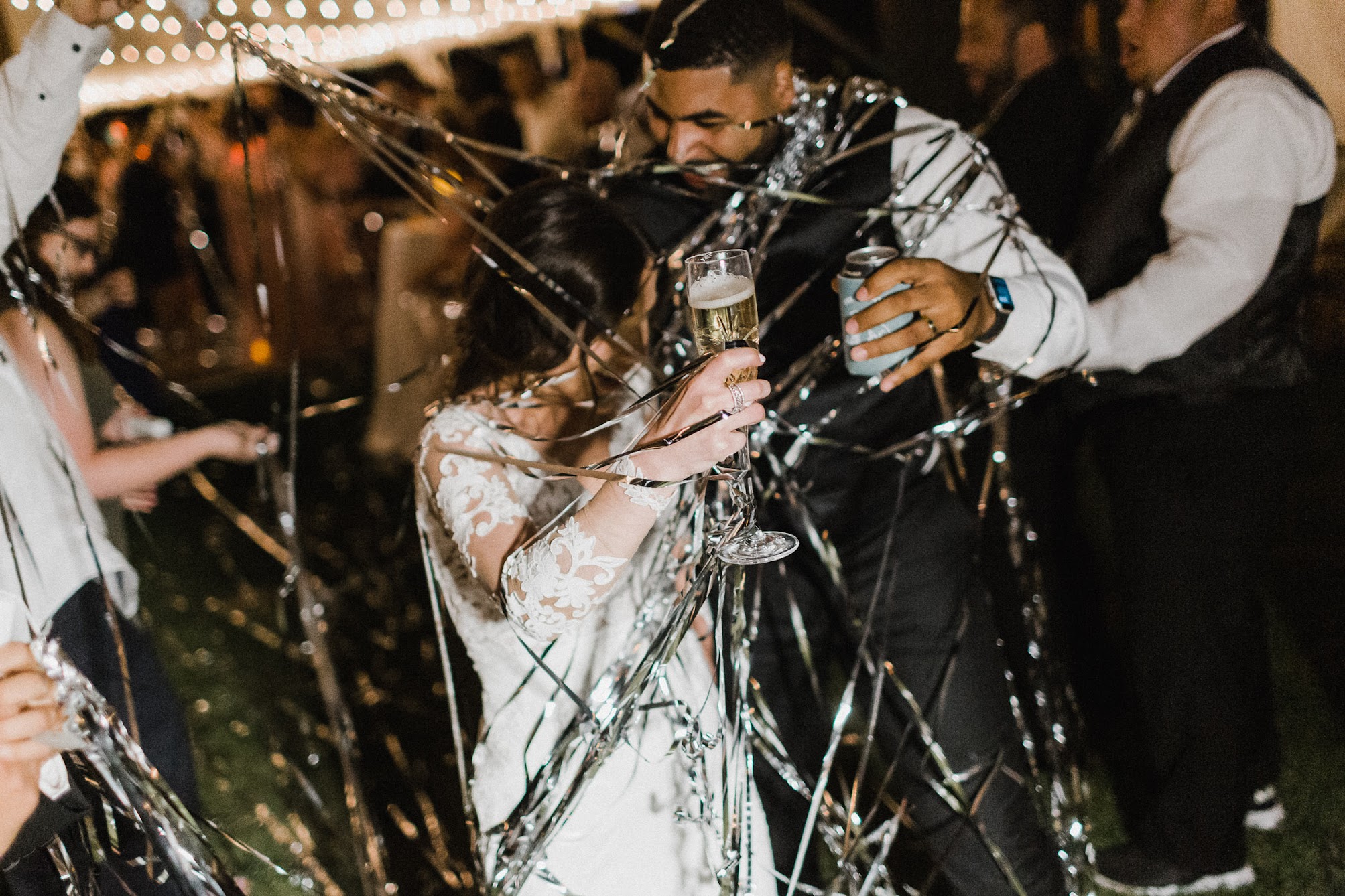 bride and groom holding their drinks their guests throw confetti at them 