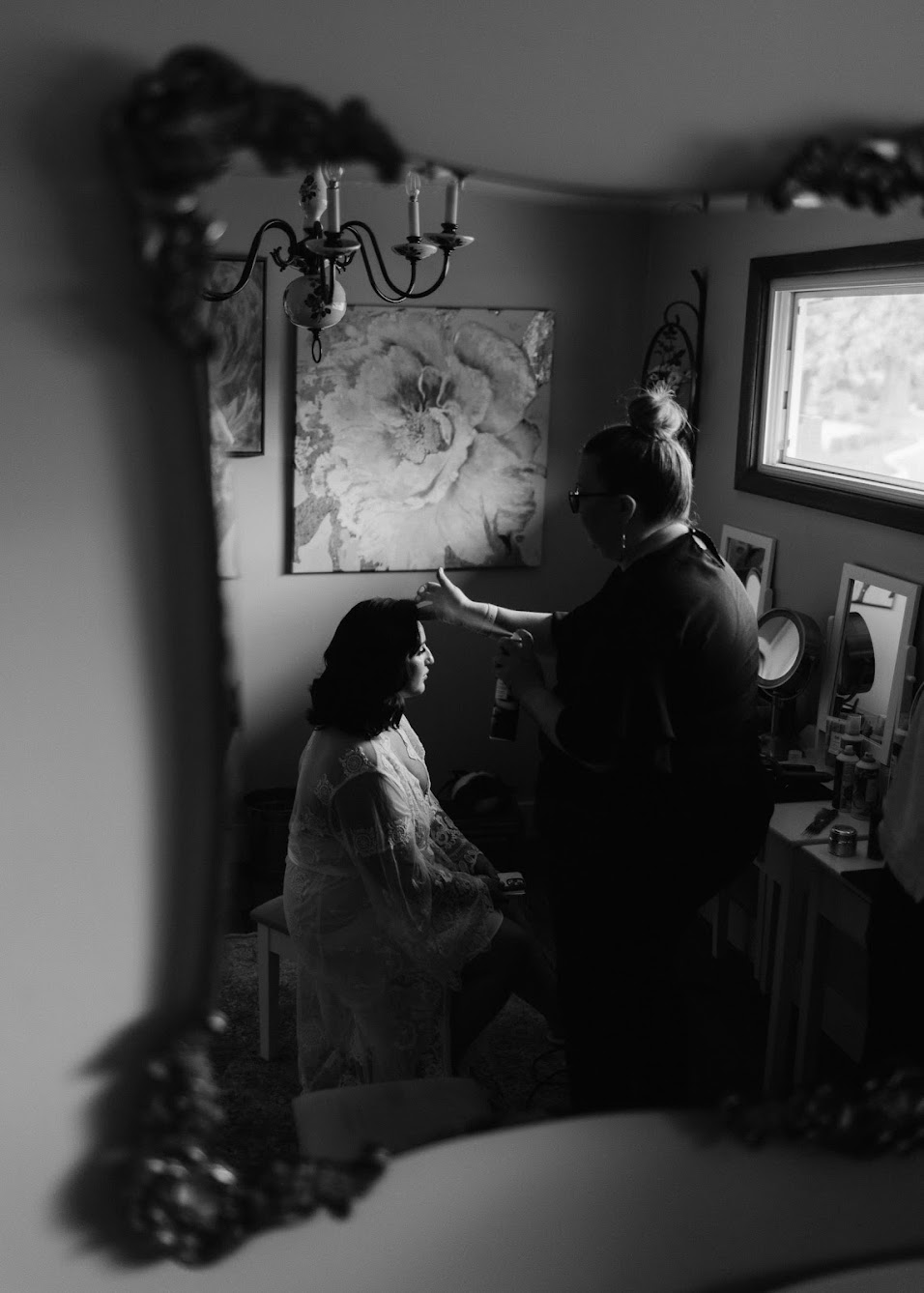 Bride getting her hair and makeup down. Sitting in a room looking at herself in a mirror while the hairstylist does her hair