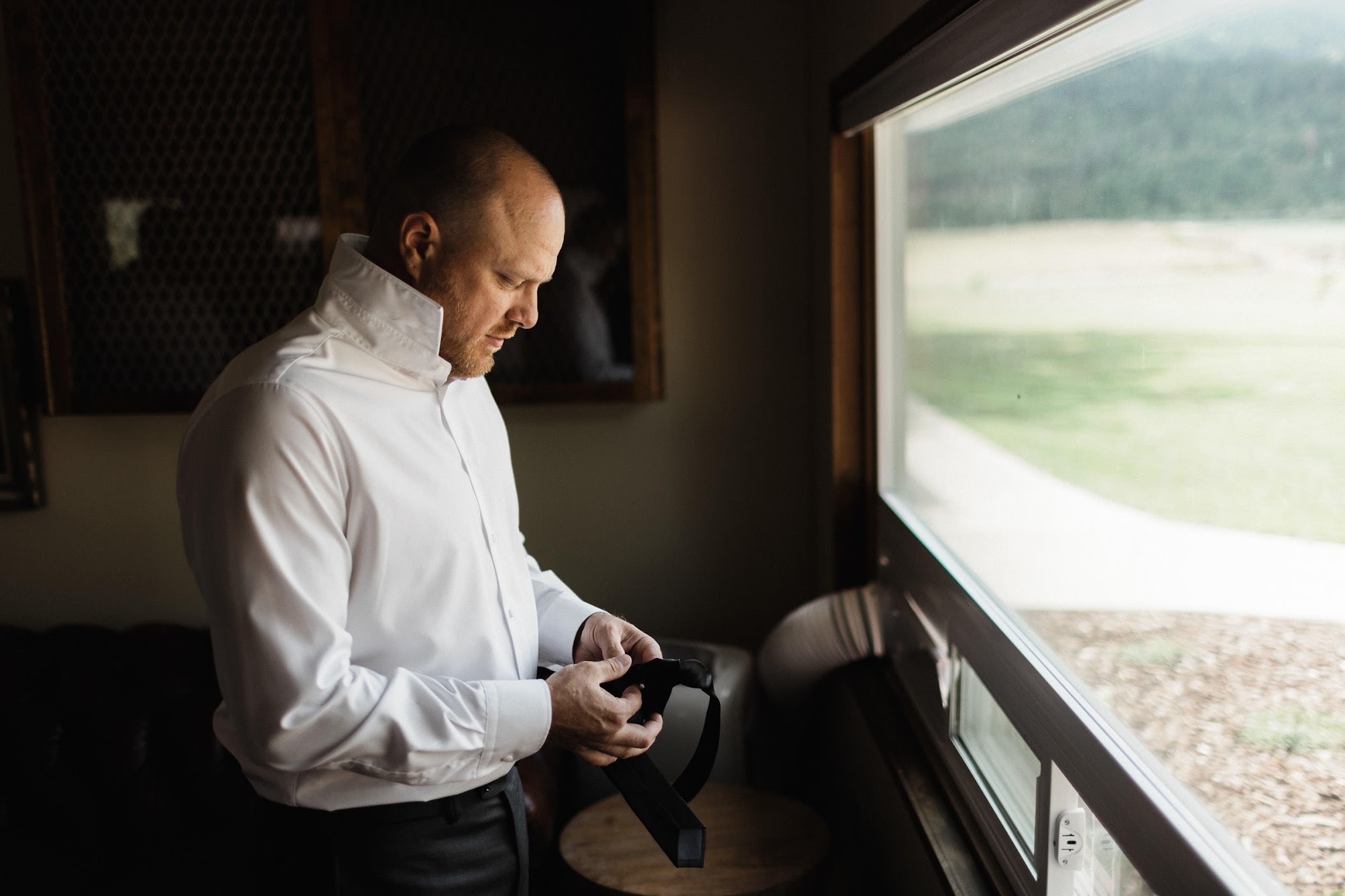 groom standing in front of a window looking at his tie.