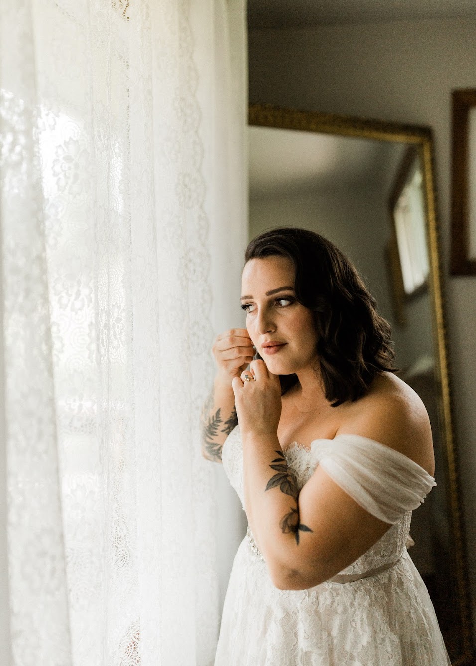 Bride putting her earrings on, staring out of the window.