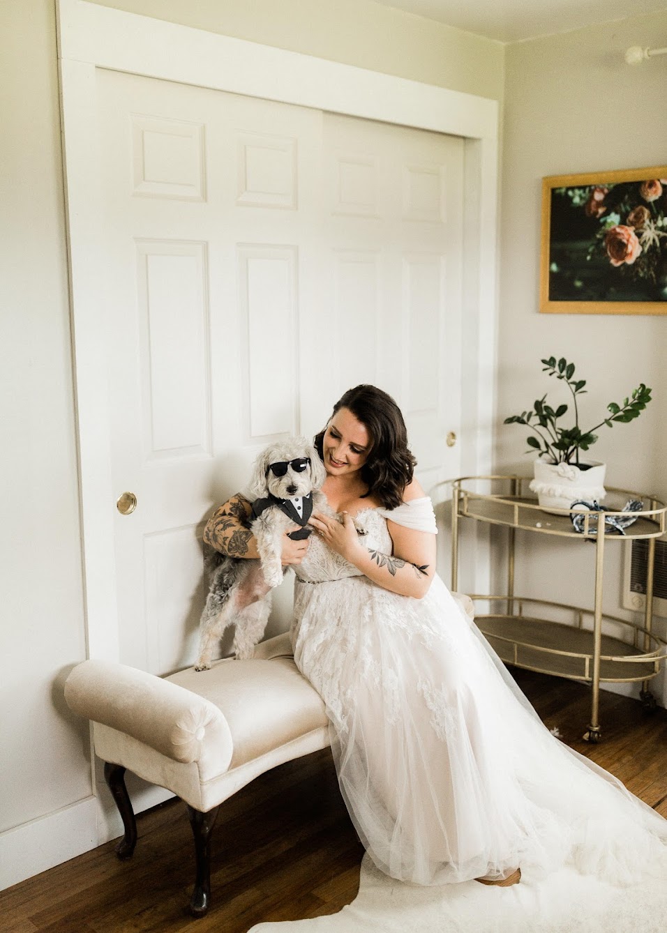 Bride sitting on a bench with her small dog, who is wearing black sunglasses and a tux vest