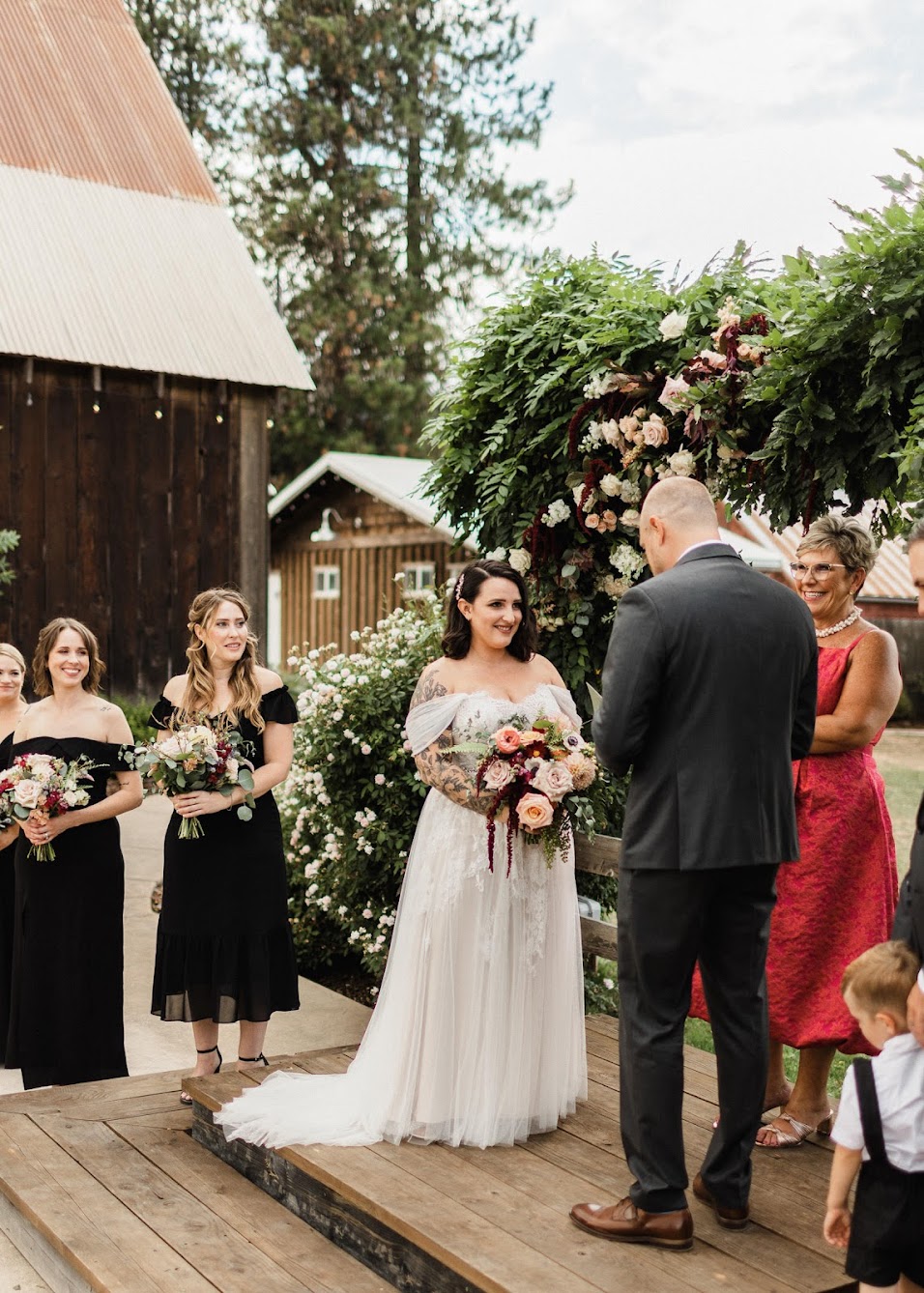The bride watches the groom as he reads his vows. Their arbor is covered in ferns and fresh roses. 