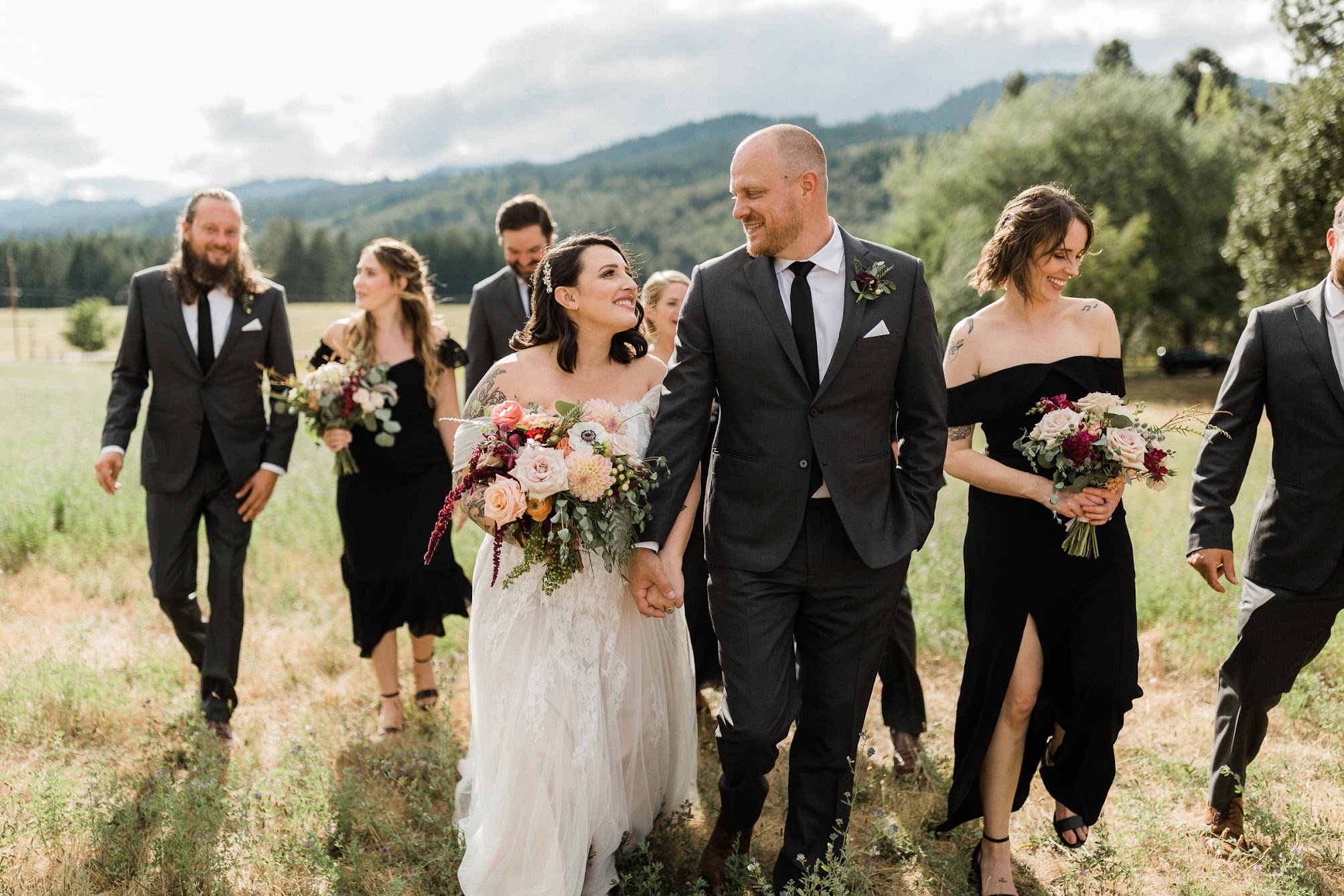 The bridal party walking in an open field. Bride and groom leading the pack while they hold hands and look at each other