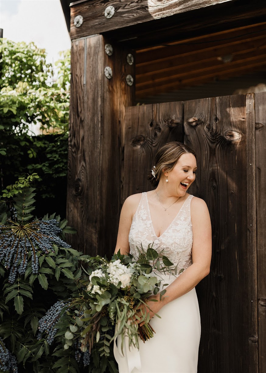 the bride outside holding her bouquet with a rustic barn behind her