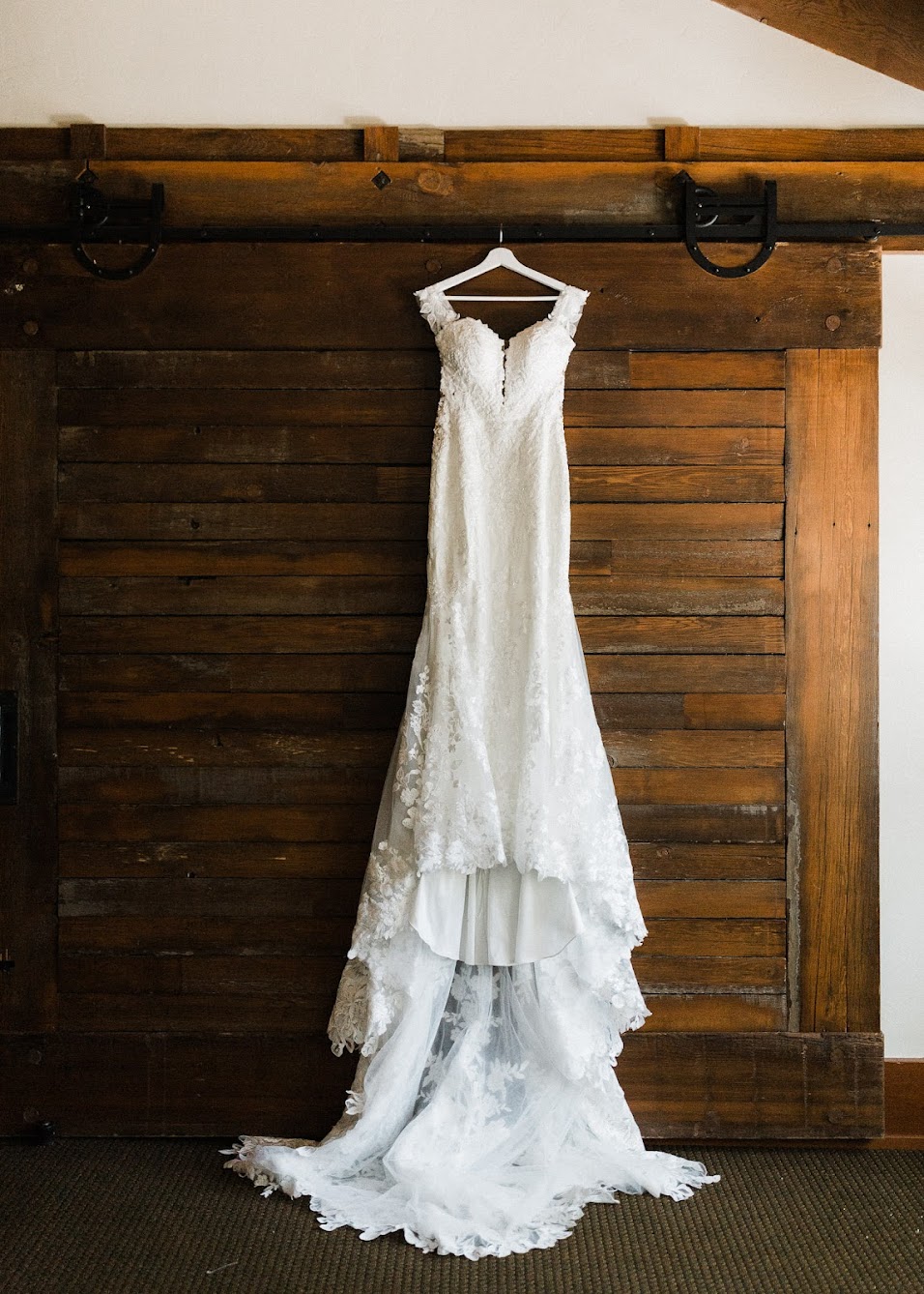 White, lacy wedding dress hanging with a wooden wall as the backdrop 