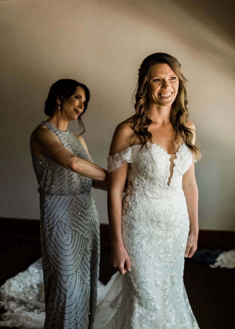 Mother of the bride helping the bride put her dress on.