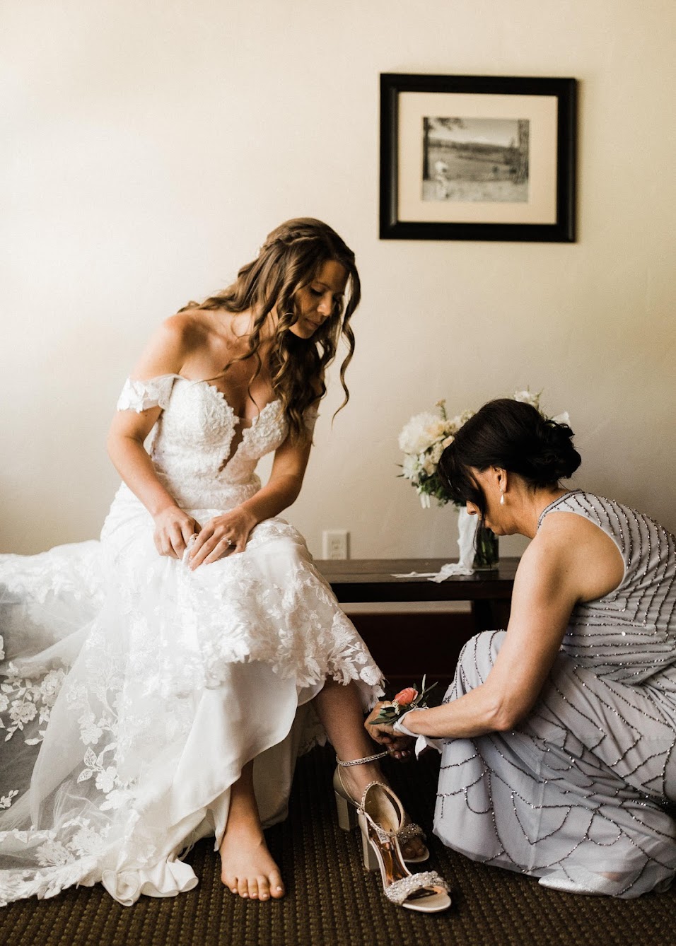 Mother of the bride helping the bride put on her shoes.