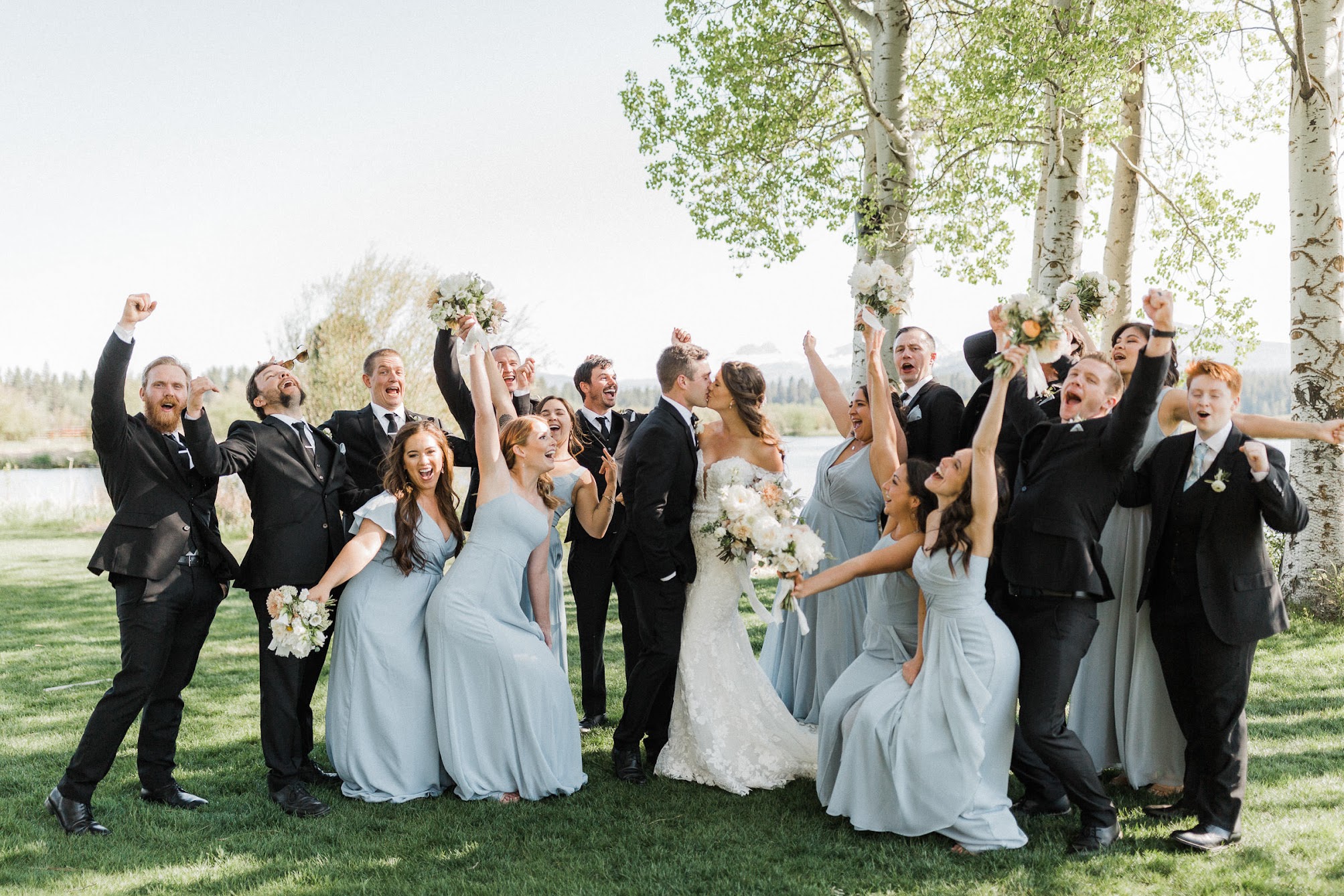bride and groom kissing while the bridal party cheers around them 