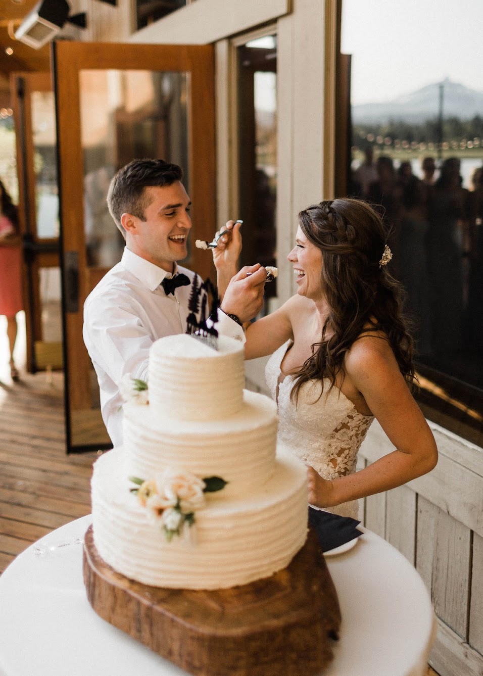 three-tiered wedding cake. The bride and groom are feeding each other a bite. 