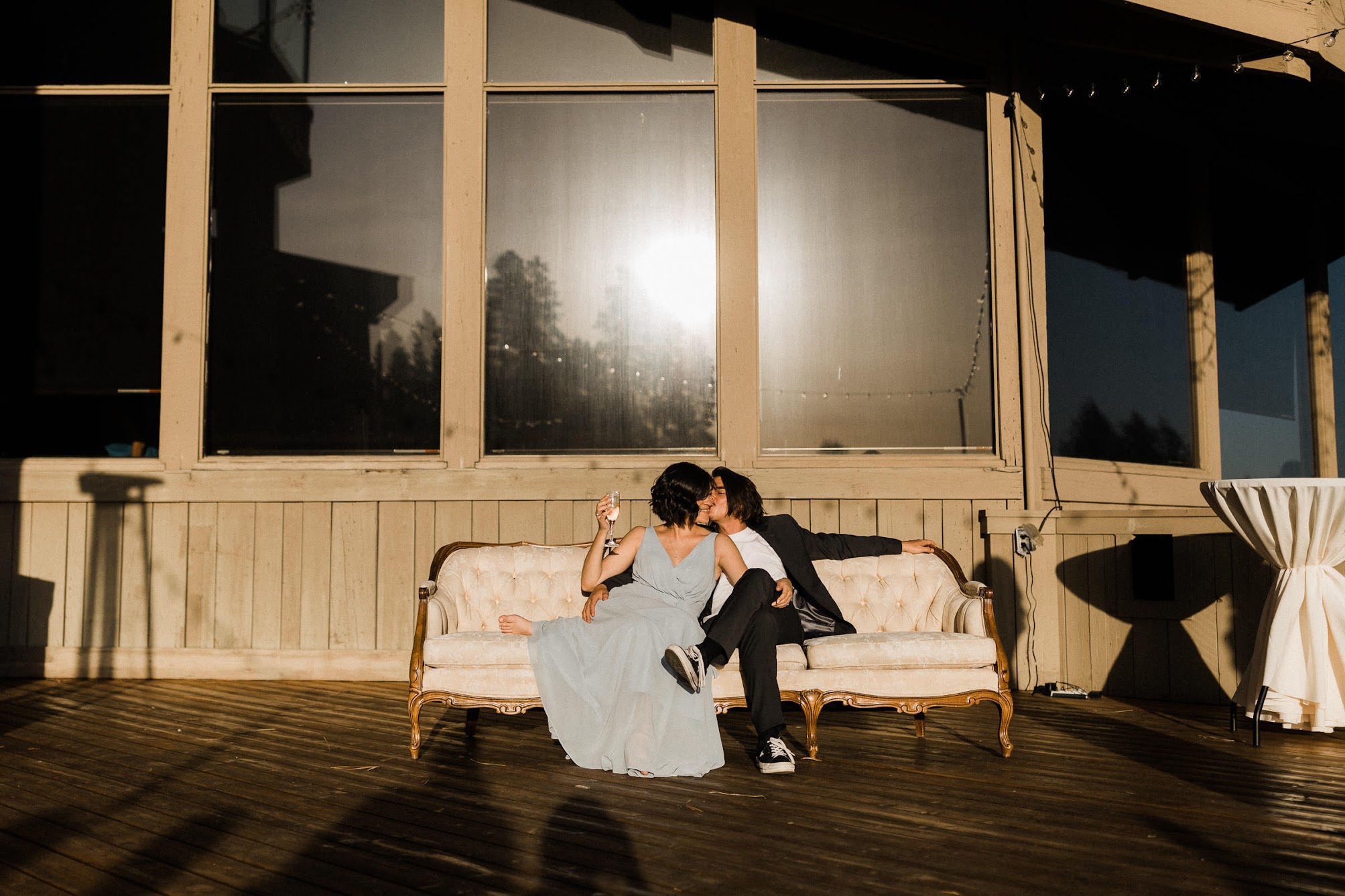 a couple sitting on a couch, he is kissing her cheek 
