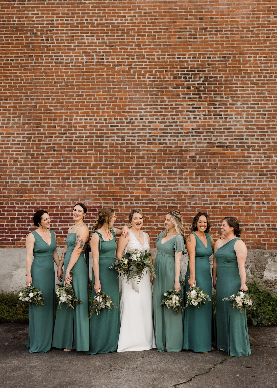 bride and her bridesmaids standing in front of a brick wall 
