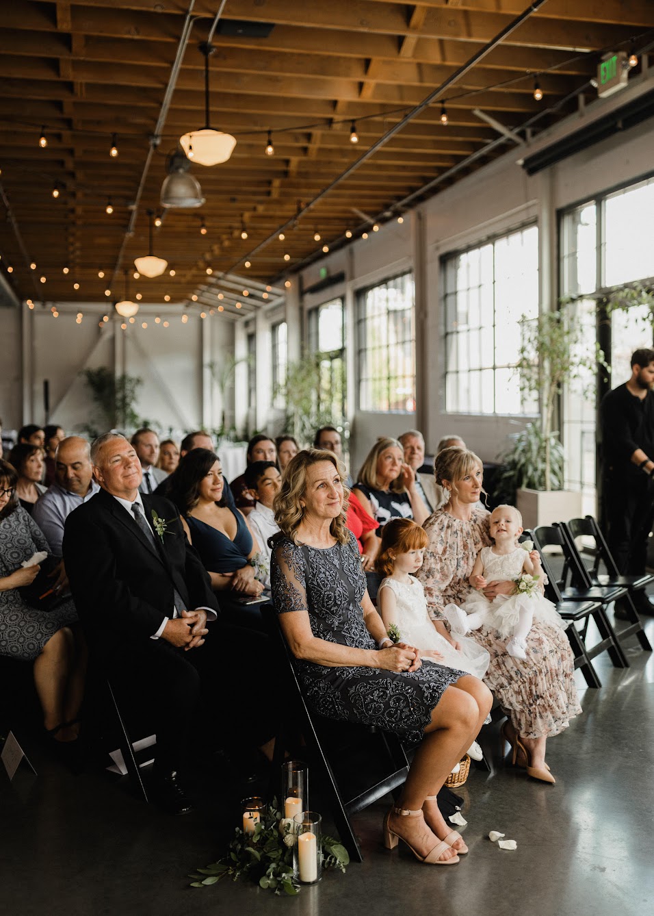 all the guests sitting down in black folding chairs watching the young couple get married 