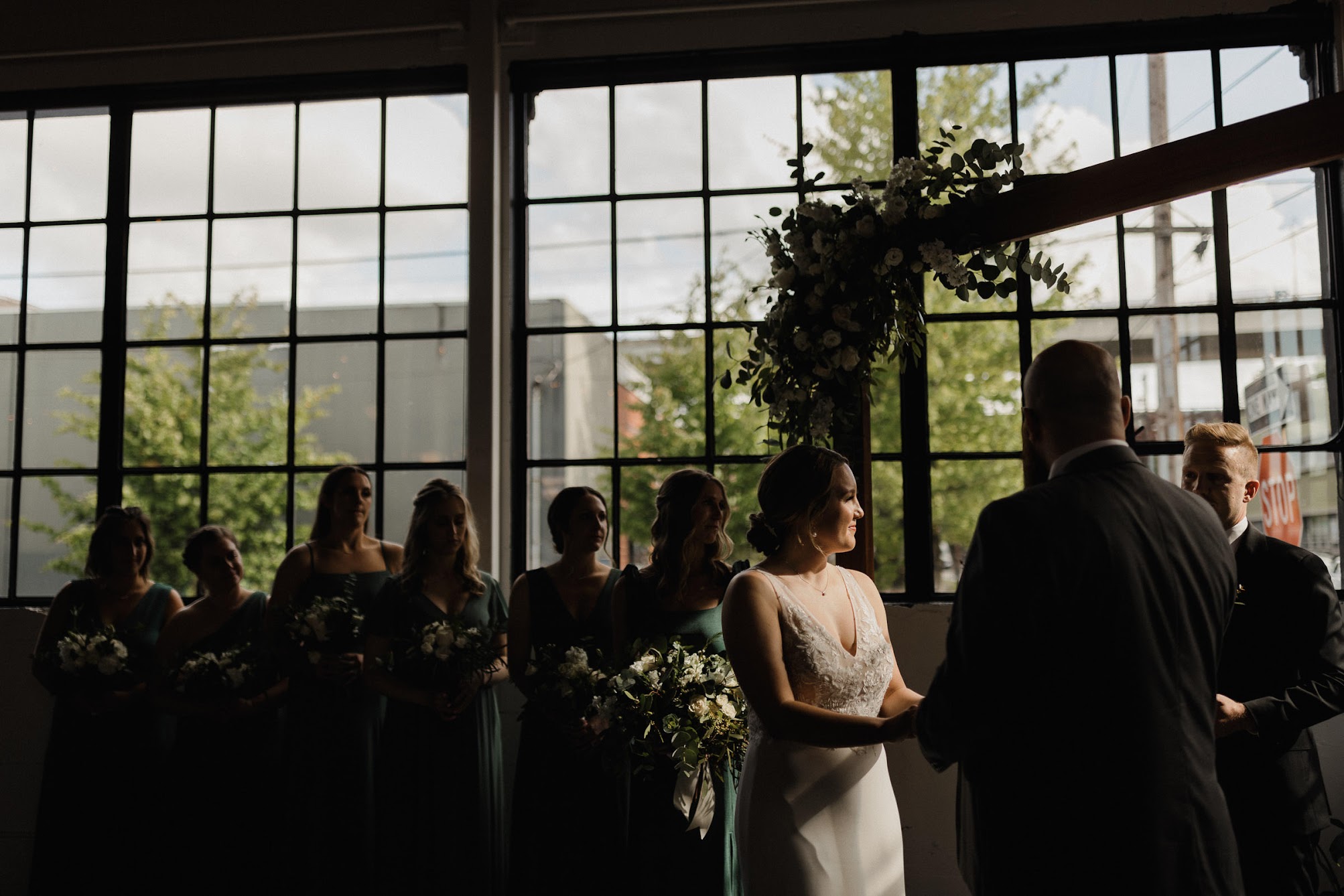 bride and groom standing at the arbor holding hands, the sunlight i just on them