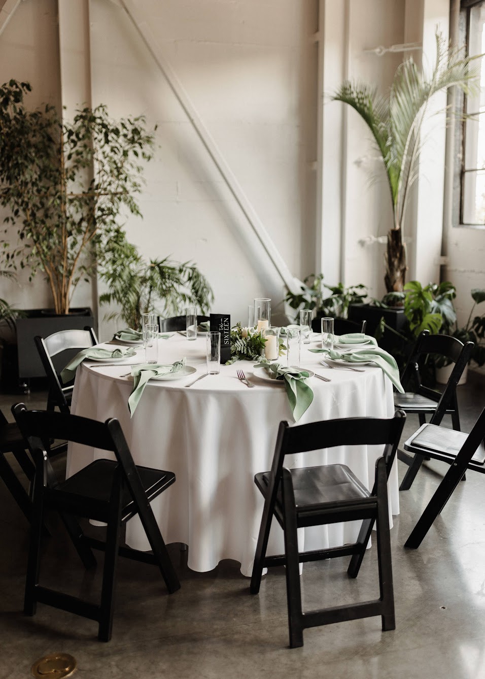 round tables with white linen and black chairs, napkins are green and folded as a knot