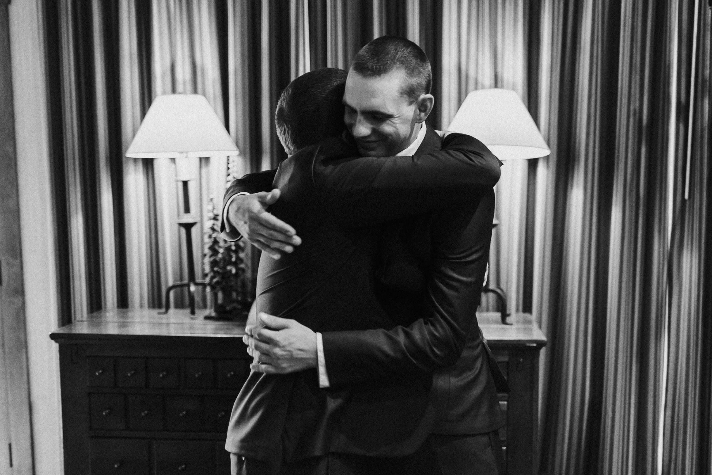 Groom and groomsman hug in hotel suite