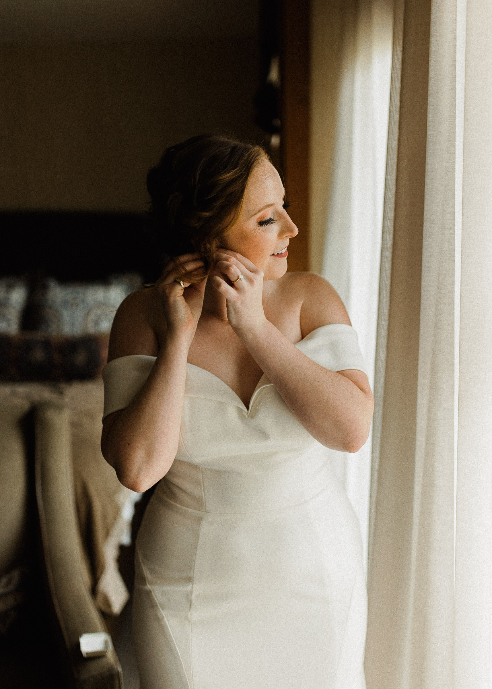Bride smiles as she puts on an earring