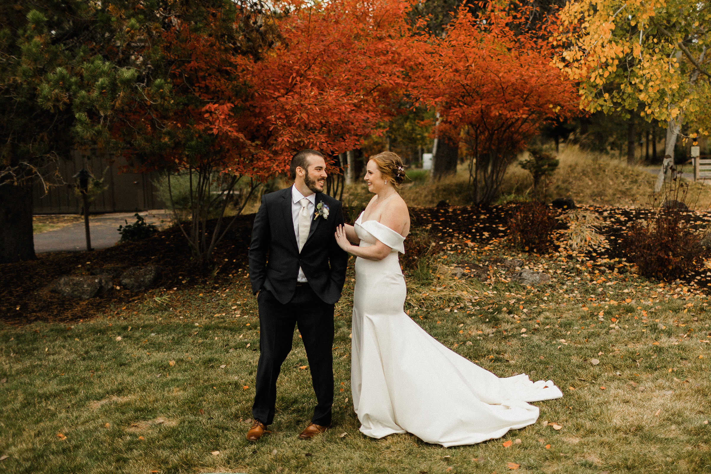 Groom smiles as he sees bride for the first time on wedding day, with red and gold foliage behind them
