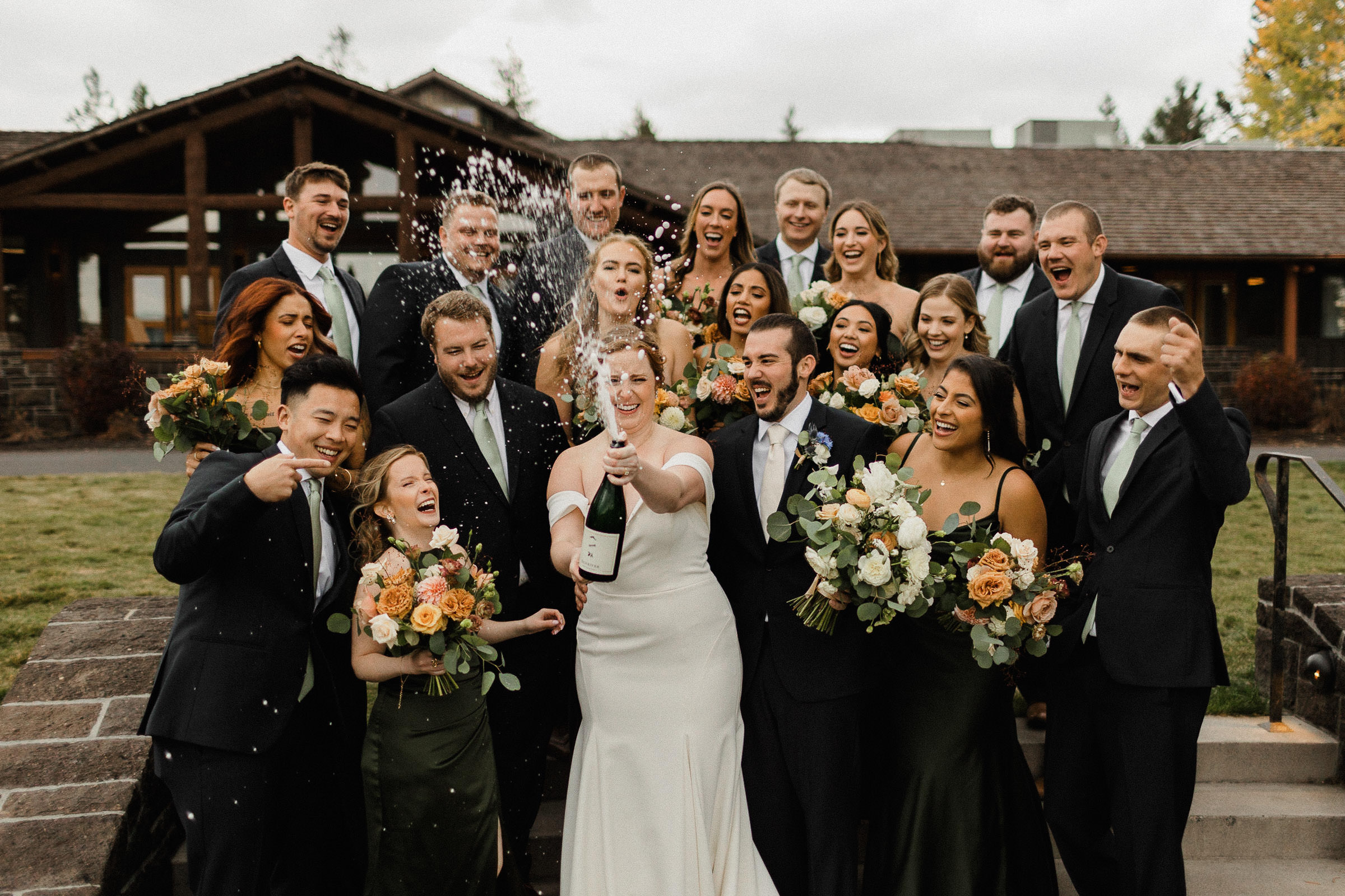 Wedding party crowds together and reacts as bride sprays champagne from a bottle