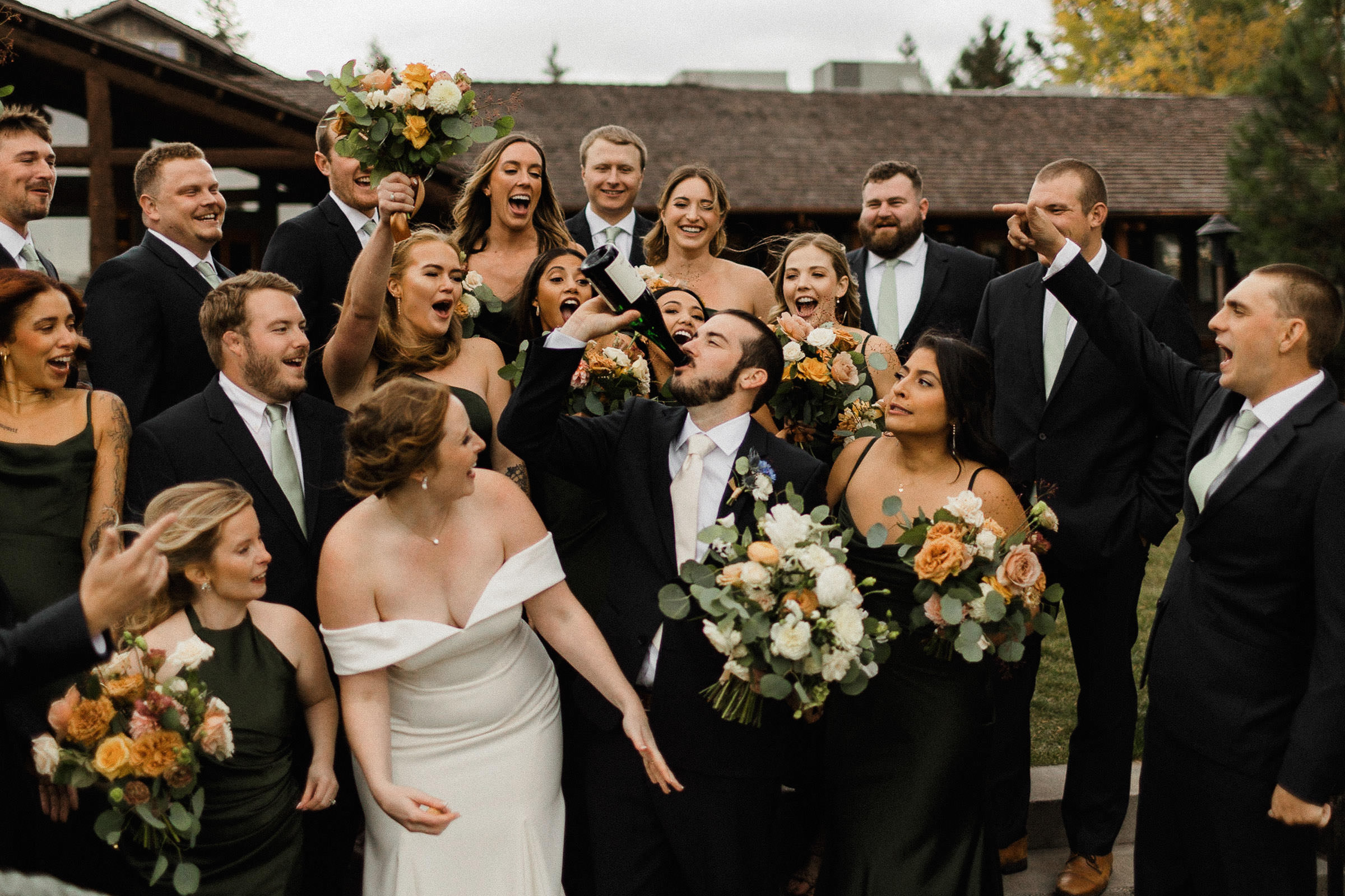Groom drinks from the champagne bottle as the wedding party cheers him on