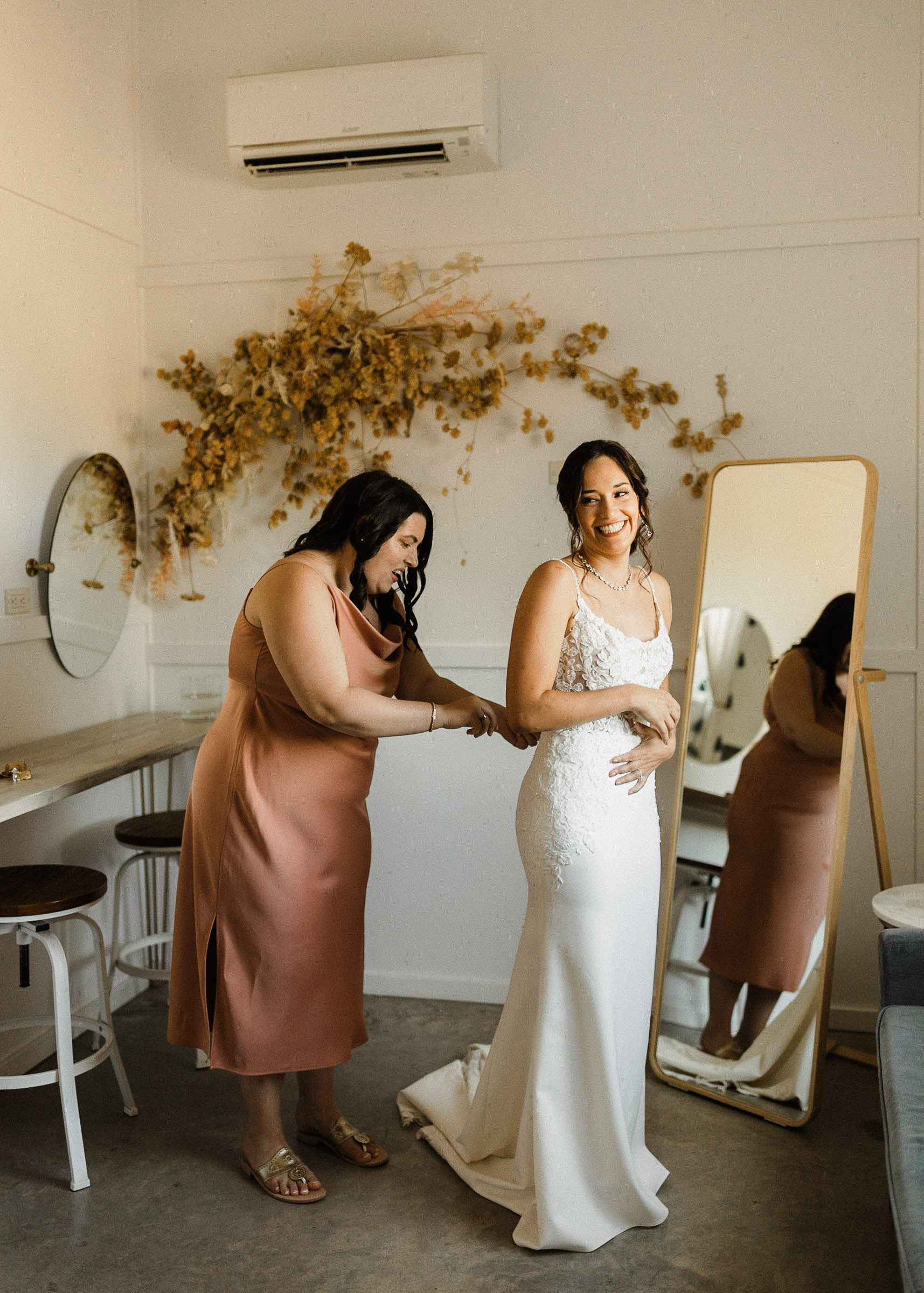 Bridesmaid buttoning back of brides dress in bridal suite