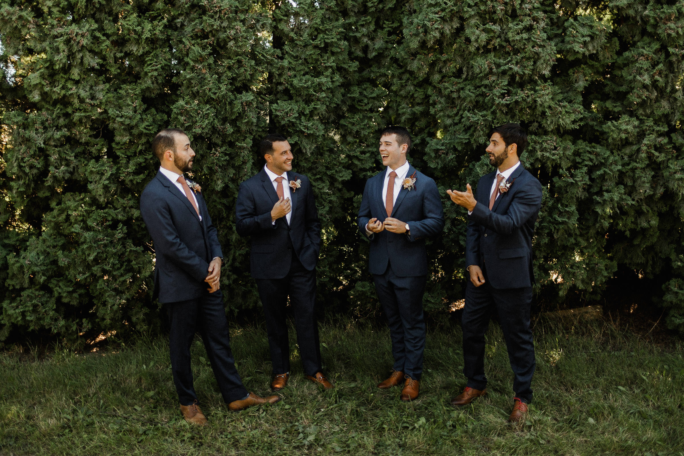 Bride and groomsmen laughing in front of hedge trees