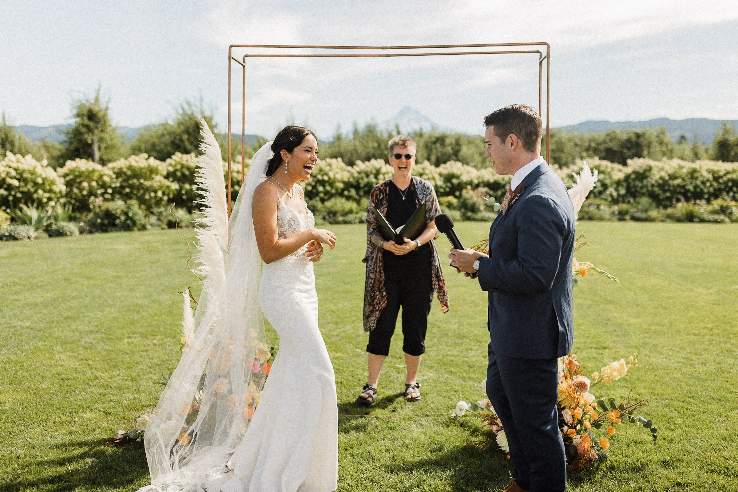 Bride smiles as groom reads vows during wedding ceremony at The Orchard